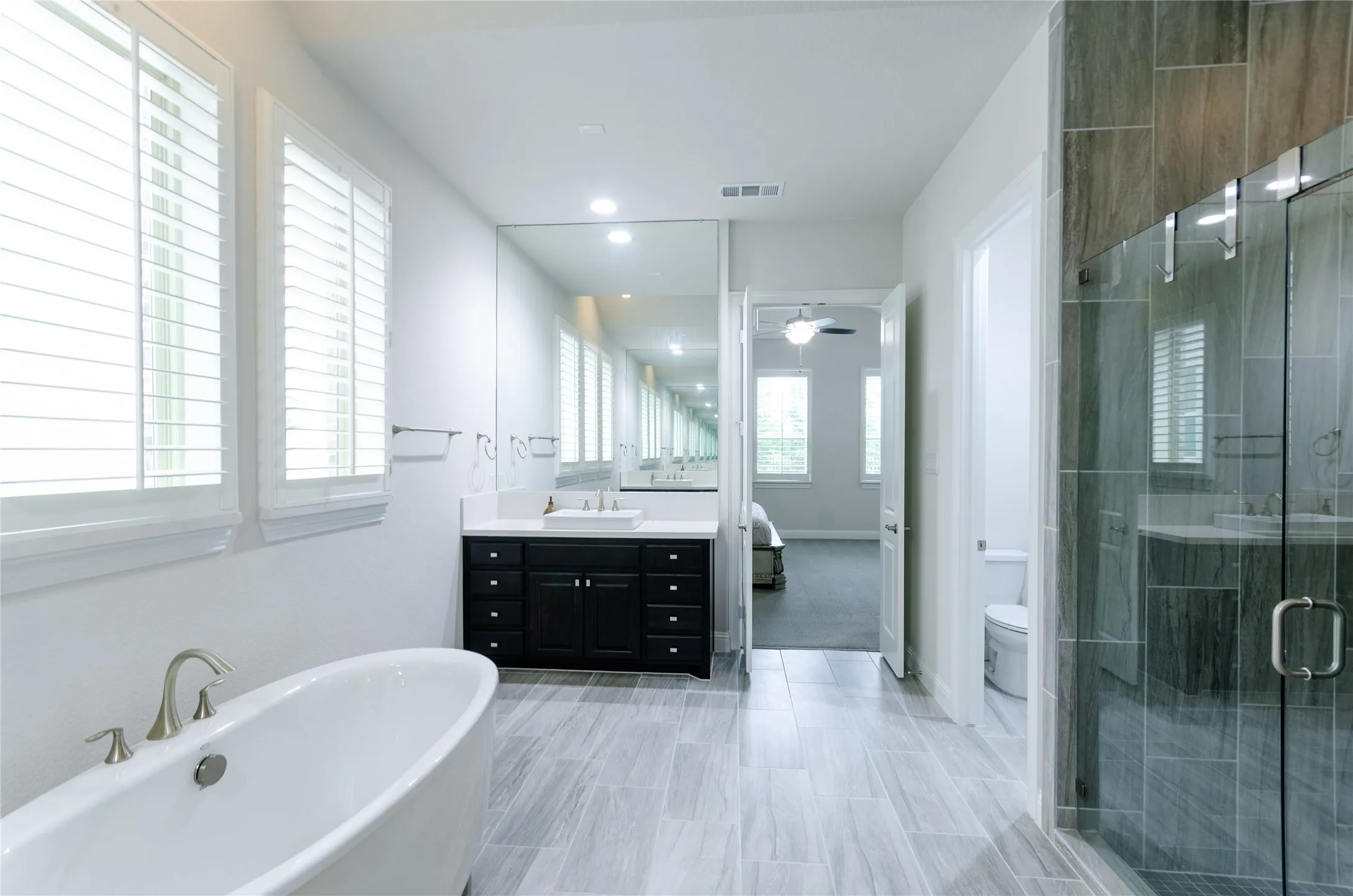 Spacious bathroom featuring a freestanding soaking tub, walk-in shower with glass enclosure, dual vanity with dark cabinetry, large integrated mirror, and wood-finish tile flooring