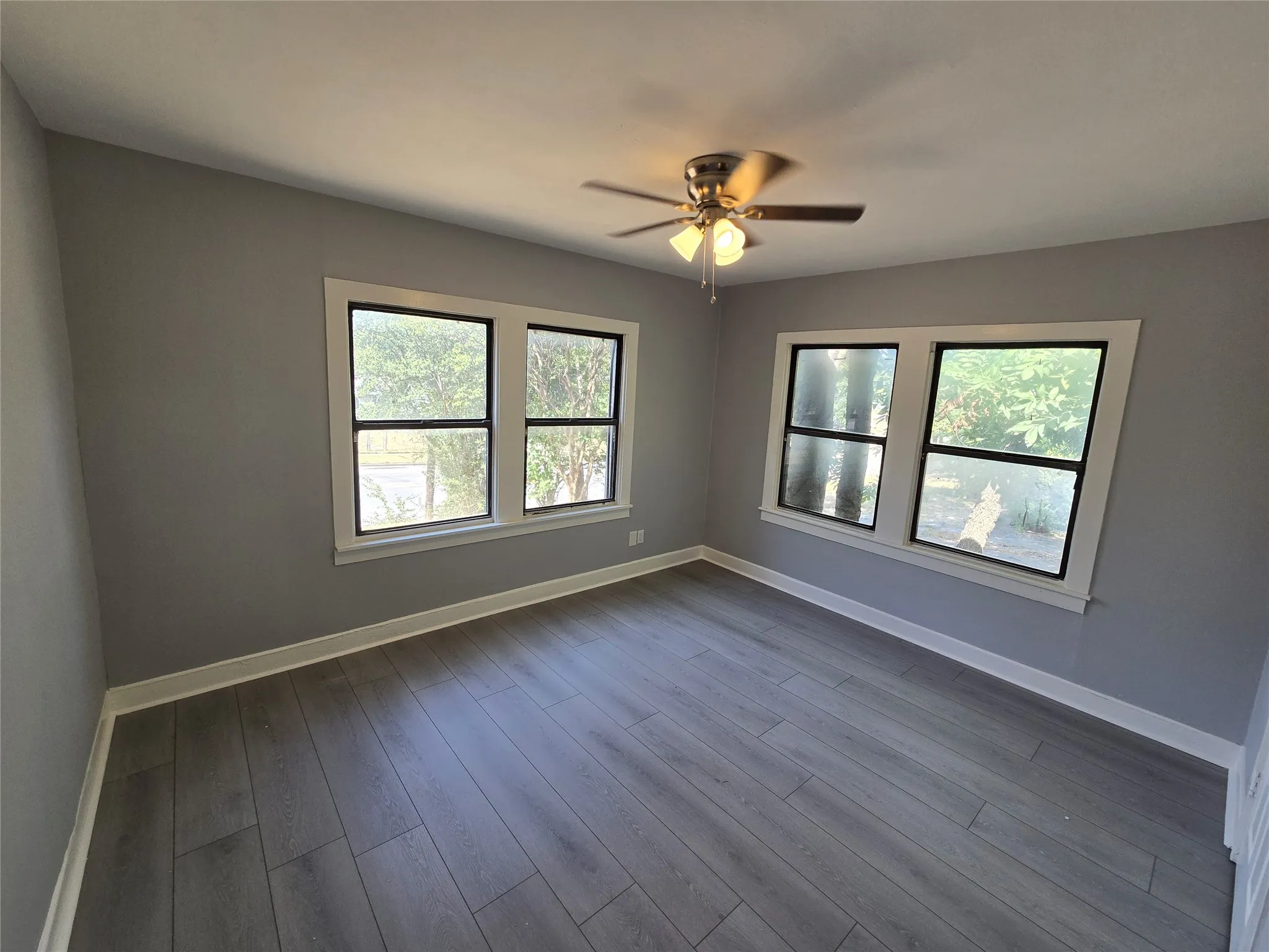 Gray wood-finish flooring, white trim, and multiple windows with white framing