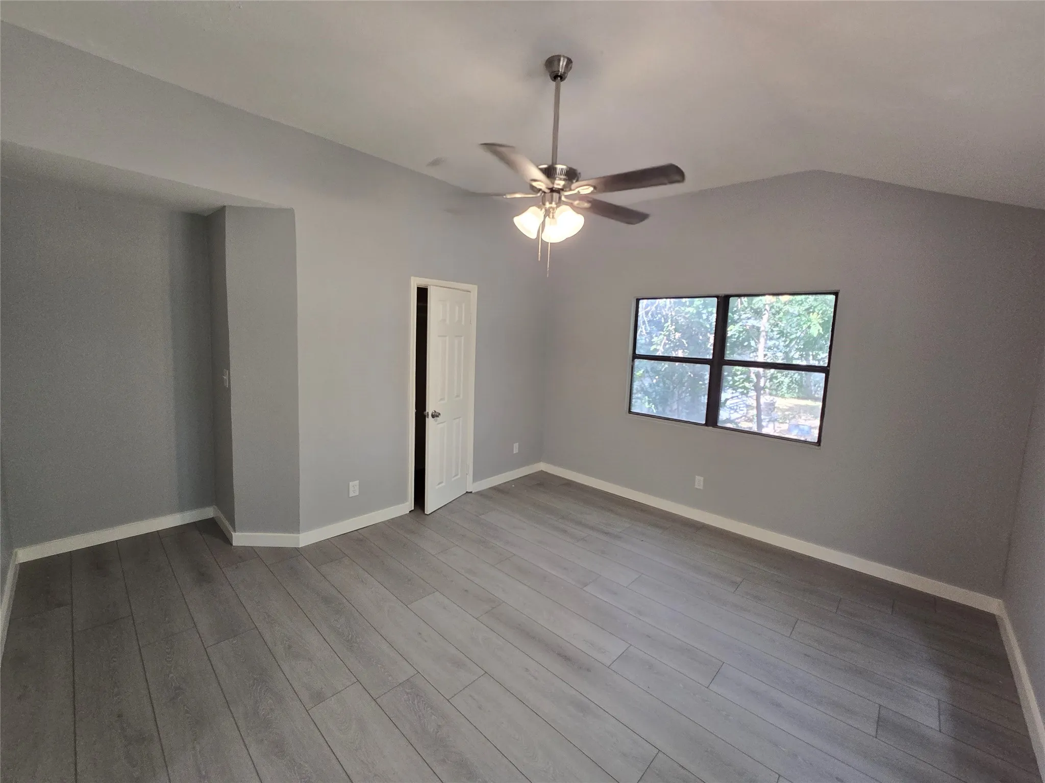 Vaulted ceilings, wood-finish flooring, ceiling fan with integrated lighting, and a paneled door