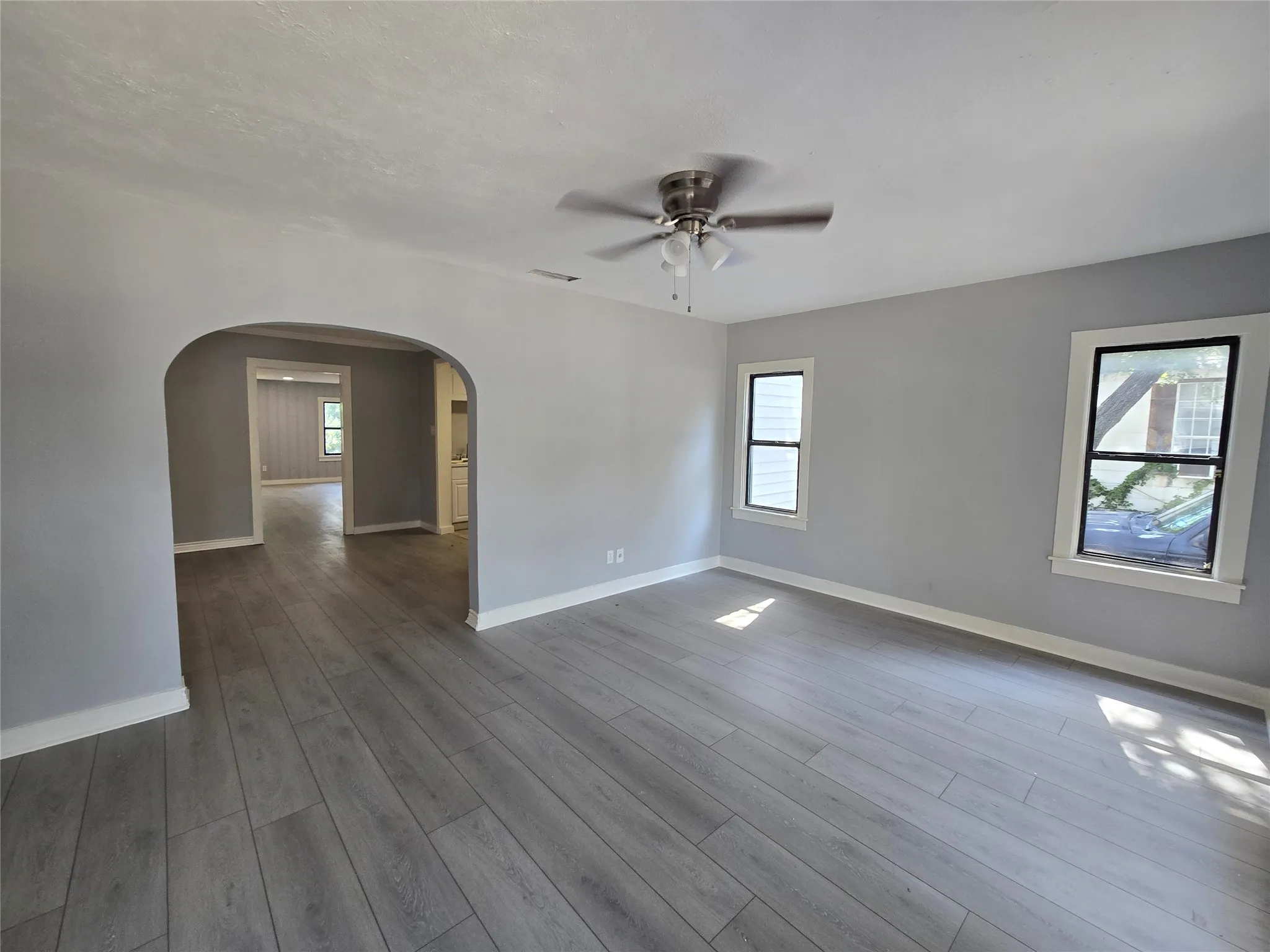 Wood-finish flooring, neutral gray wall tones, ceiling fan with brushed nickel finish, and white trim windows