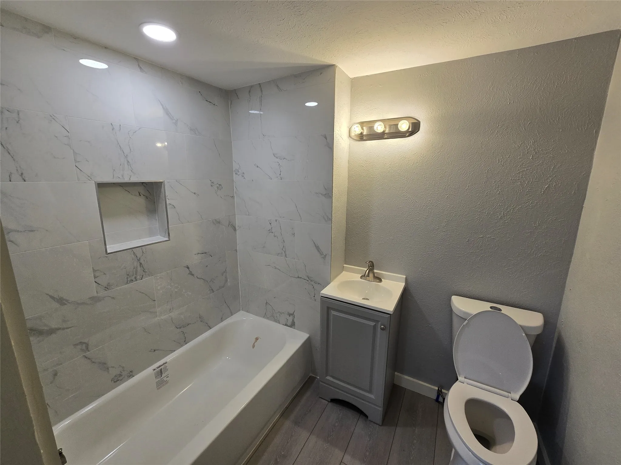 Bathtub with tiled surround, recessed shower niche, and overhead lighting