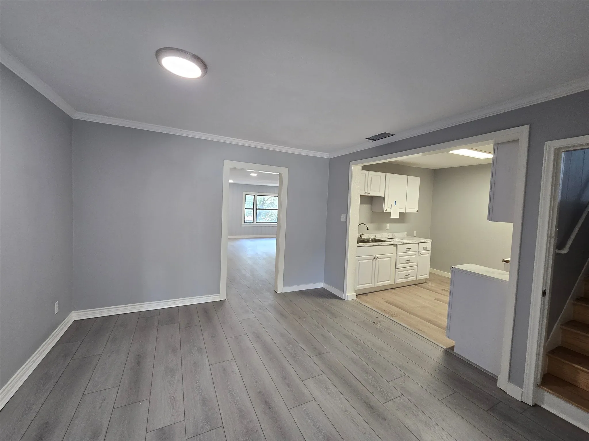Wood-finish flooring throughout, recessed ceiling lighting, kitchen area with white cabinetry, and a light wood-finish staircase