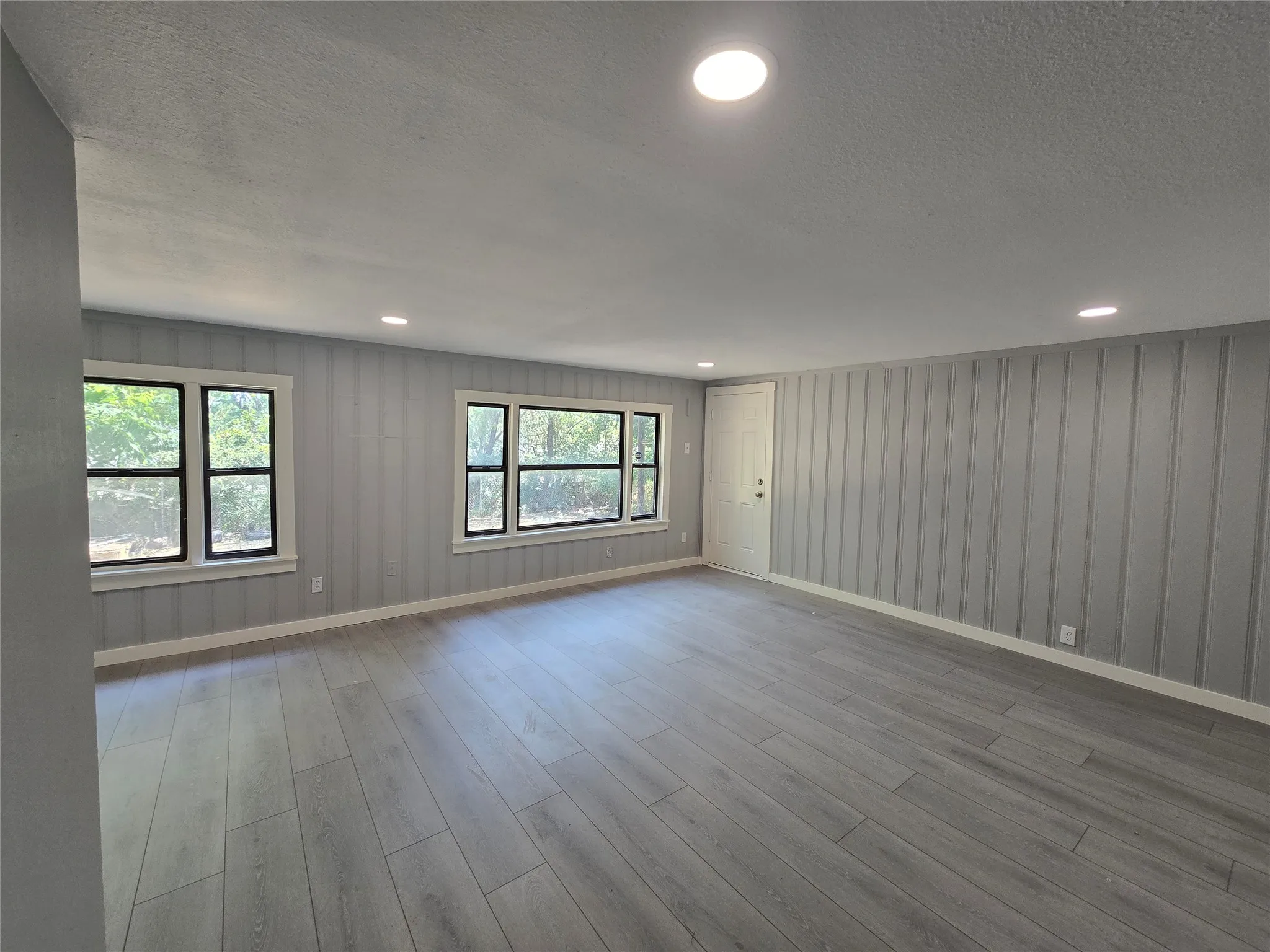 Spacious room with wood-finish flooring, recessed lighting, multiple windows, and board and batten wall detailing