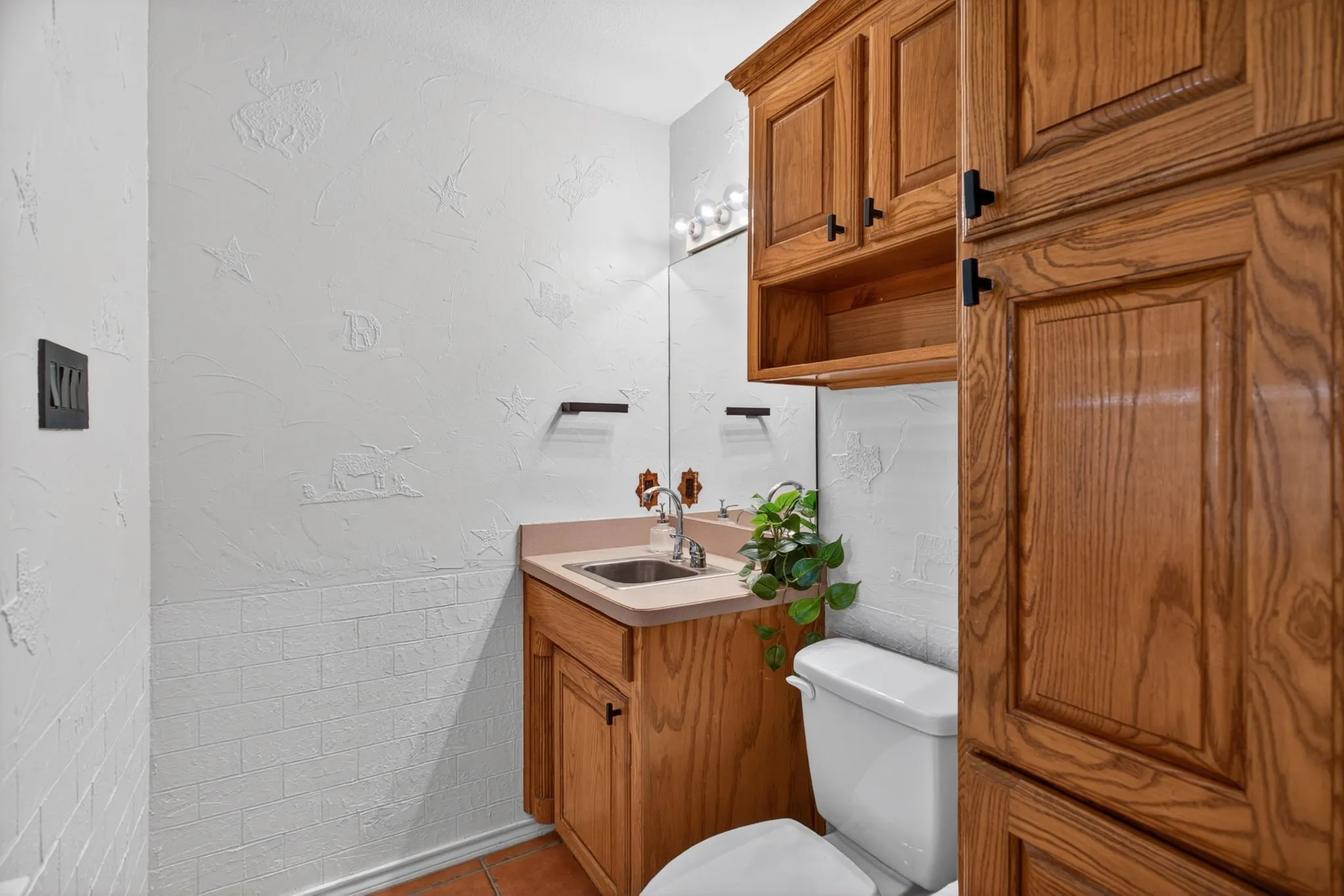 Nifty half bath with oak cabinets, good storage, and embossed western details on the walls.