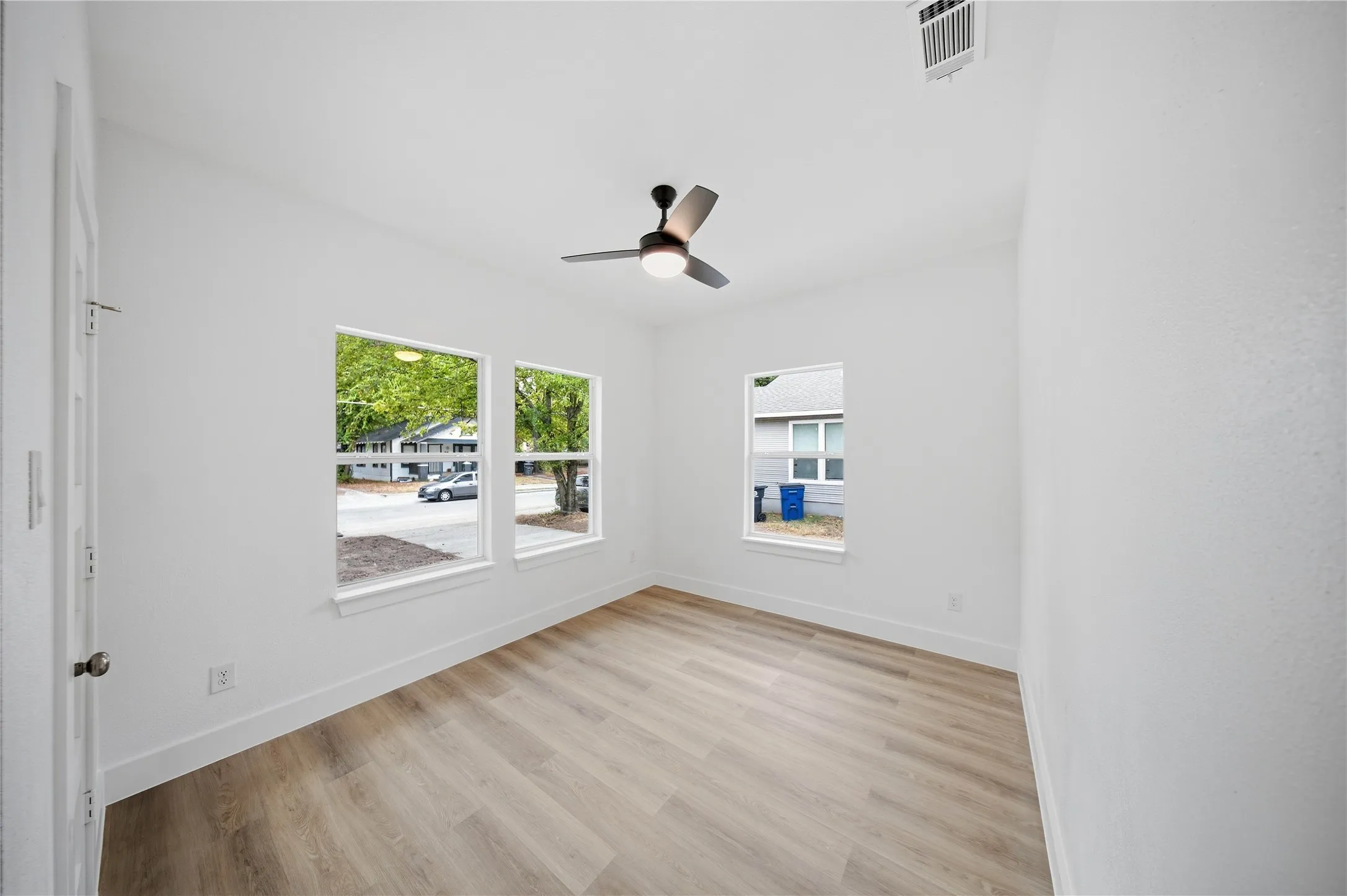 Light-filled room featuring wood-finish flooring, multiple windows, a ceiling fan with integrated lighting, and white walls
