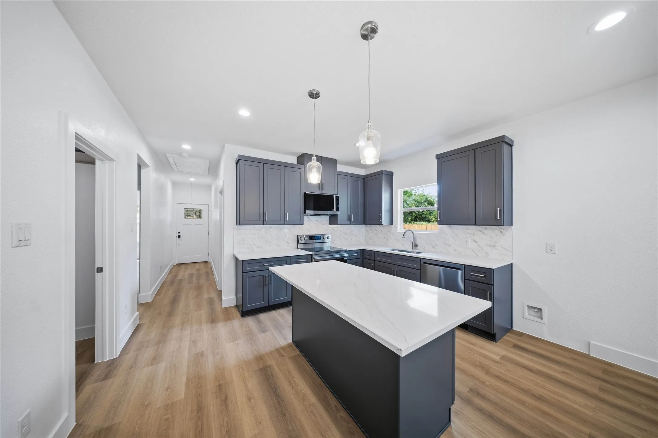 Kitchen featuring dark cabinetry, white countertops, stainless steel appliances, a white tile backsplash, and wood-finish flooring
