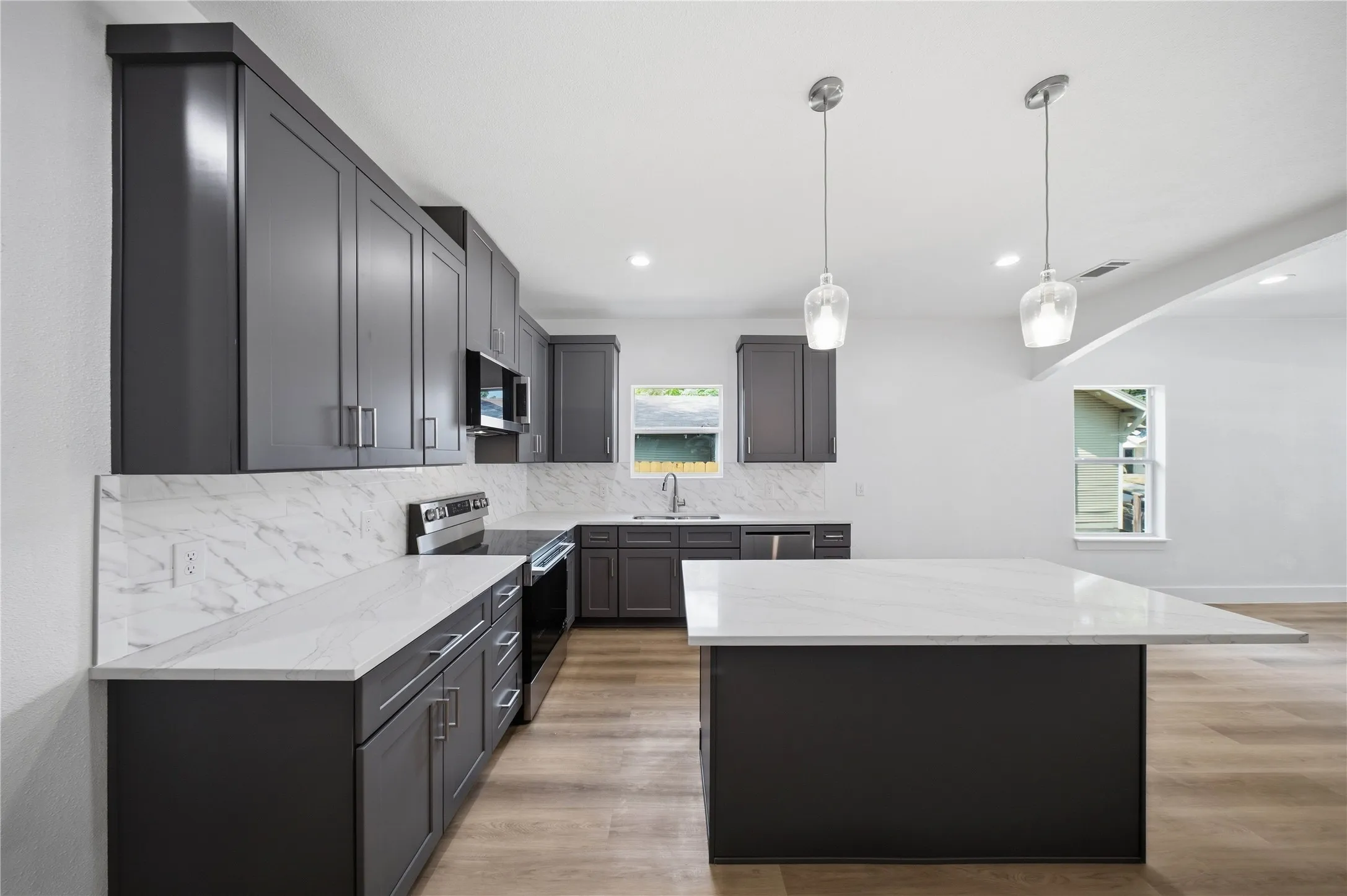 Kitchen featuring dark cabinetry, white countertops, white backsplash, stainless steel appliances, and a central island with pendant lighting