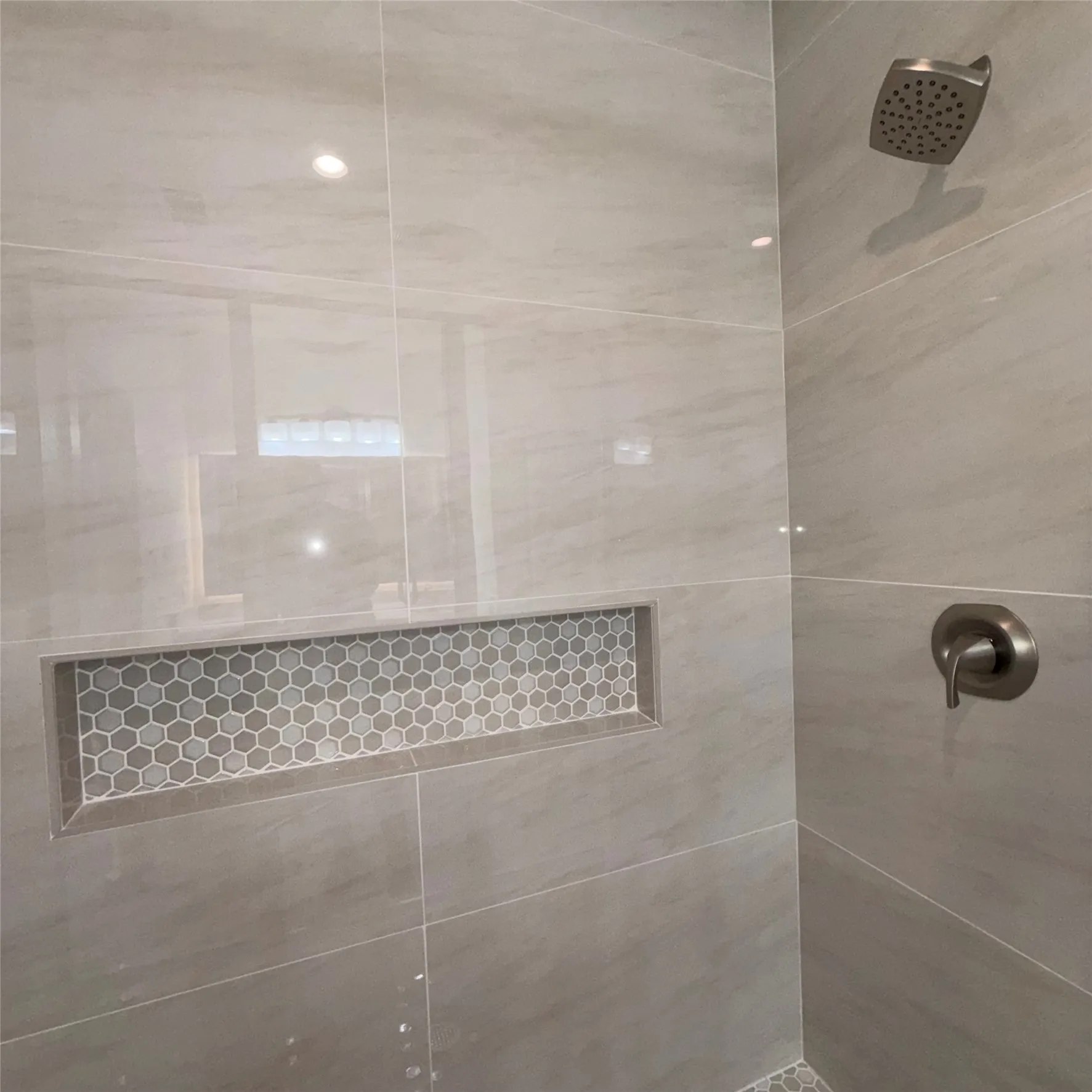 Shower stall featuring large format neutral tile, a built-in hexagonal mosaic niche, a rain showerhead, and a brushed metal single-lever control