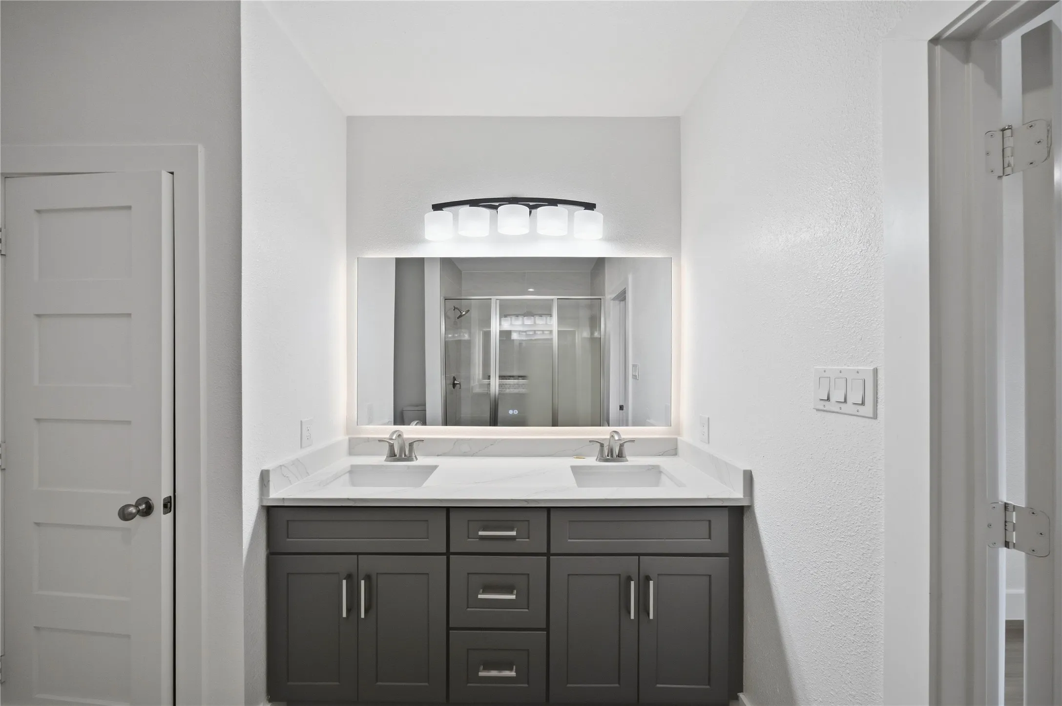 Dual sinks, stone-finish countertop, dark wood-finish vanity, illuminated mirror, and modern lighting fixture