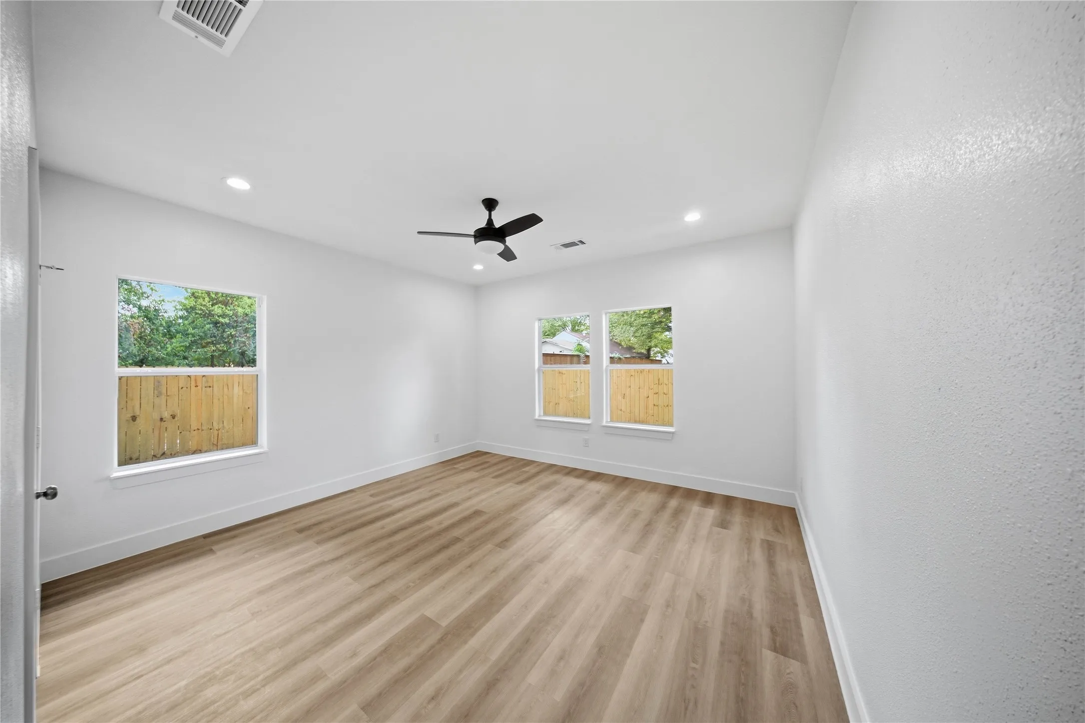 Spacious room featuring wood-finish flooring, two windows, recessed lighting, and a ceiling fan
