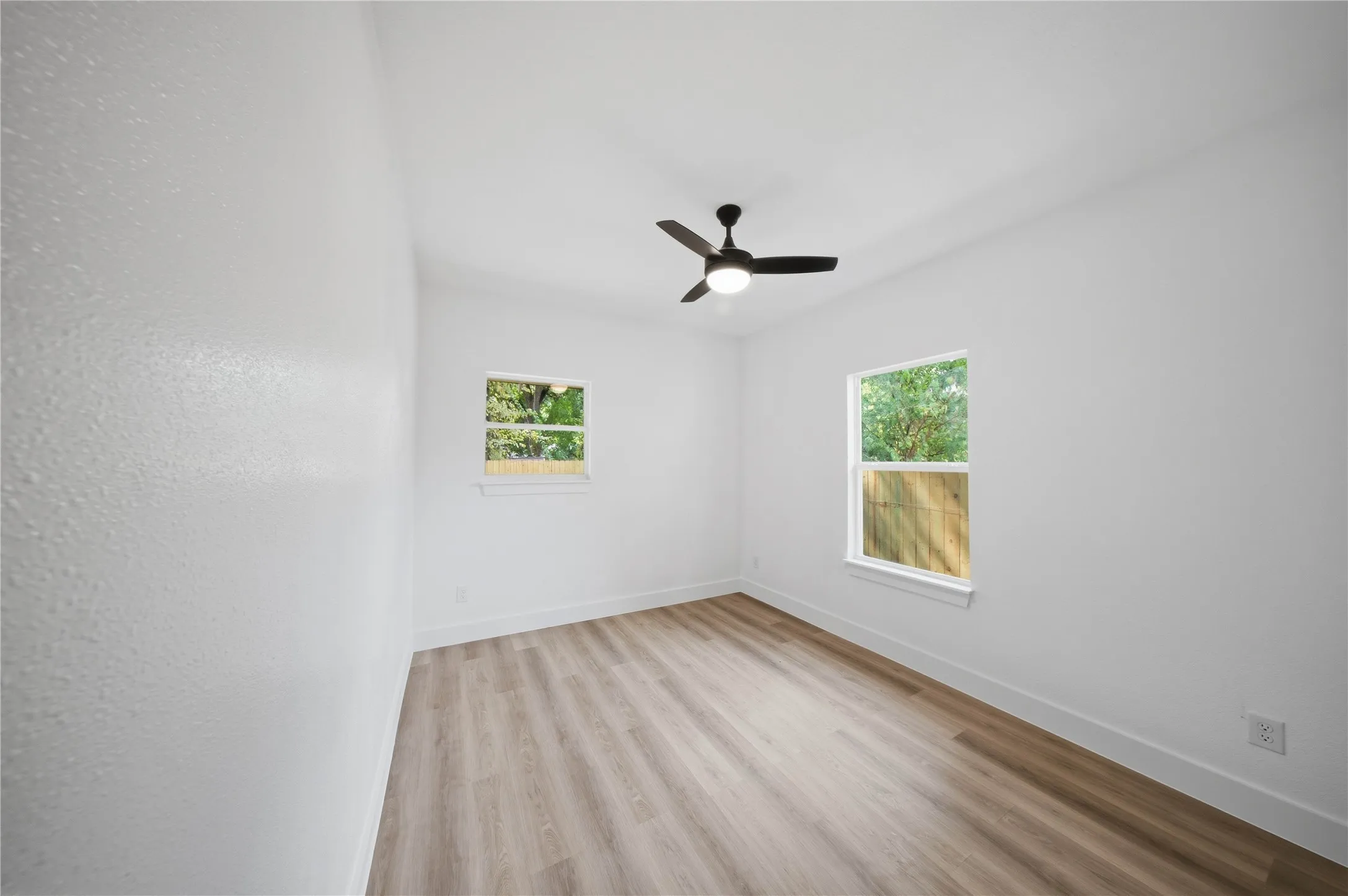 Wood-finish flooring, white walls, two windows, and a ceiling fan with integrated lighting