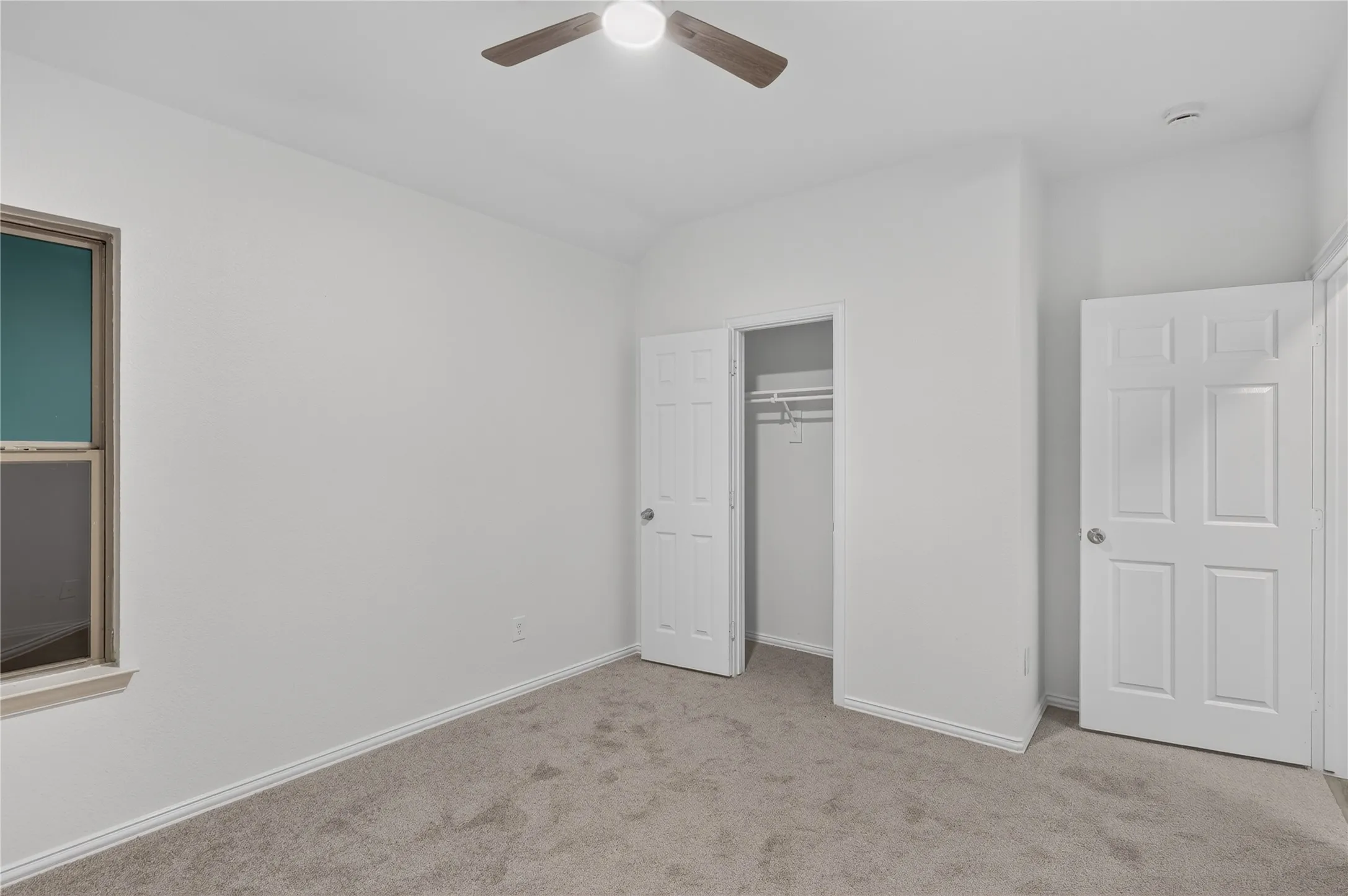 Carpeted room featuring a ceiling fan with integrated lighting, a window with a wood-finish frame, and two panel doors
