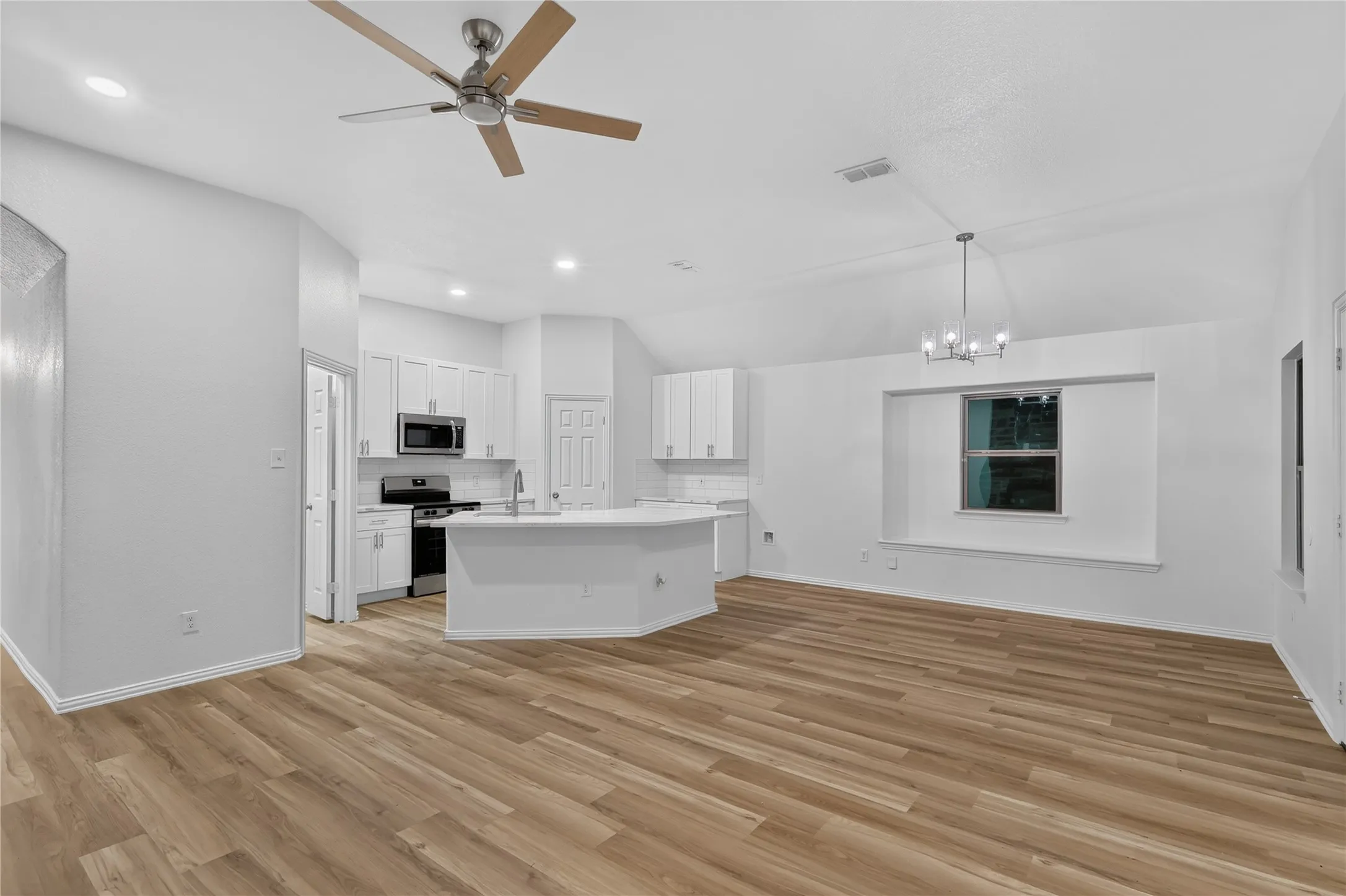 Open-concept living space with wood-finish flooring, white cabinetry, stainless steel appliances, a breakfast bar, and a window seat