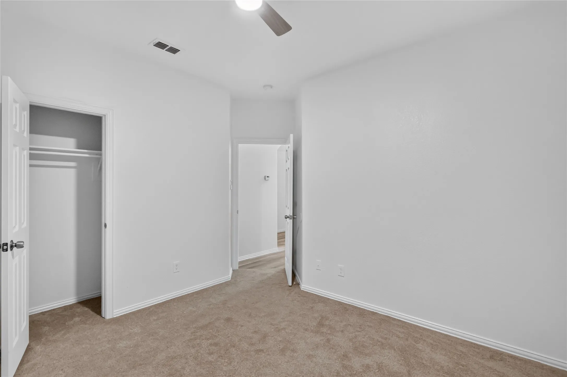Neutral carpet flooring, white walls, closet with hanging rod, and a ceiling fan