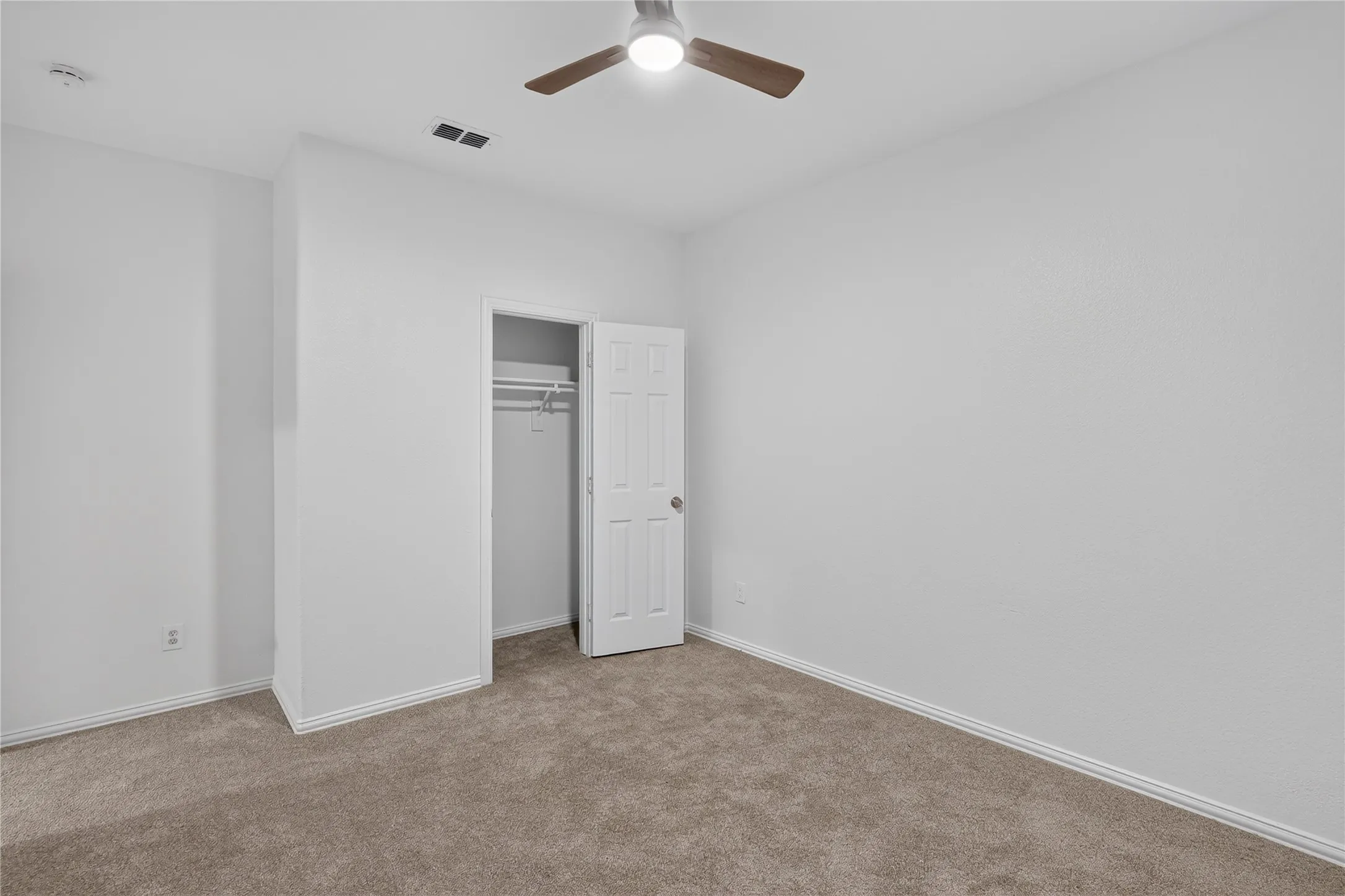 Neutral carpet flooring, white walls, built-in closet with shelving, ceiling fan with integrated lighting