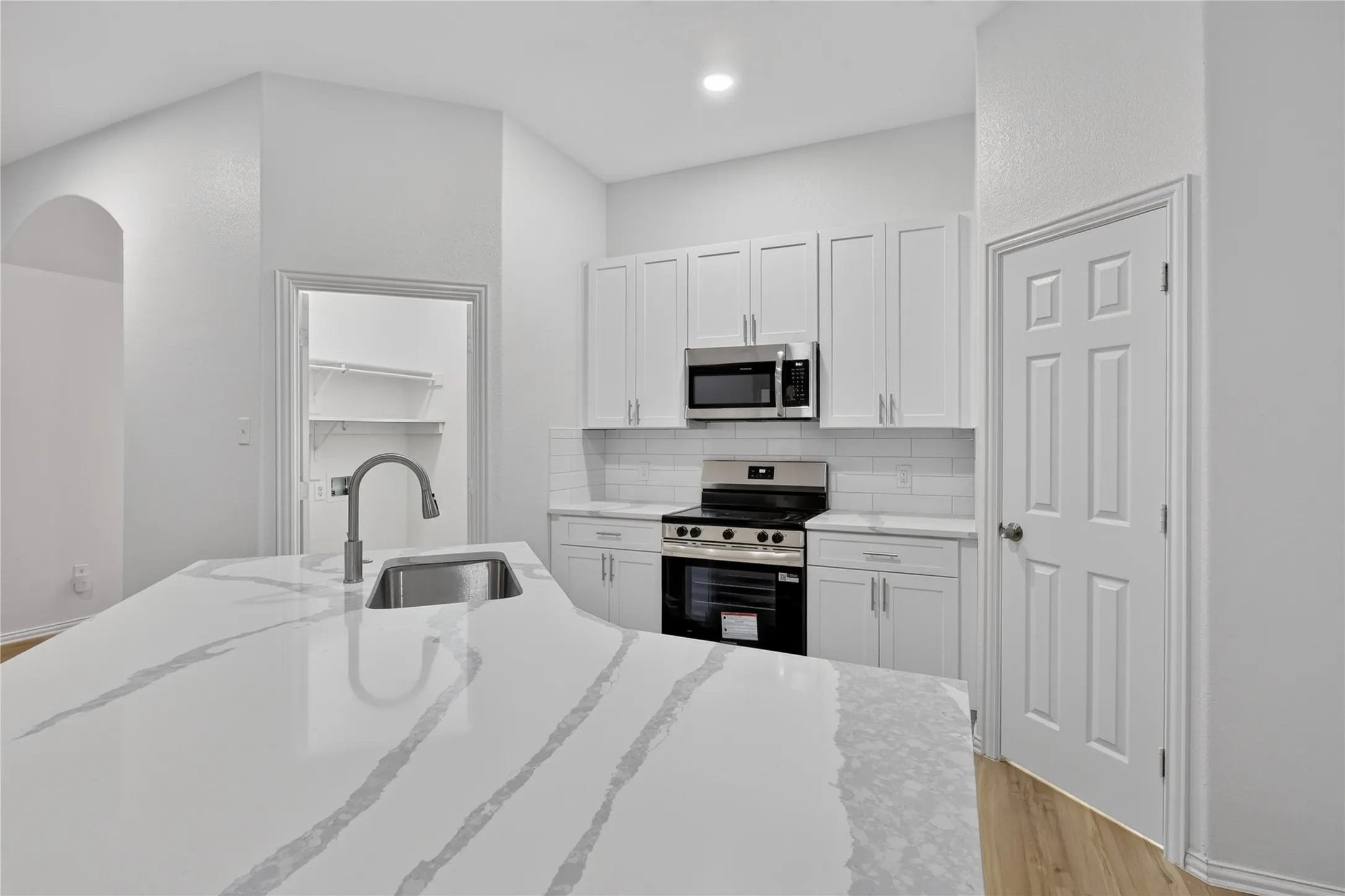 Kitchen featuring a large island with an undermount sink, stainless steel appliances, white cabinetry, and subway tile backsplash