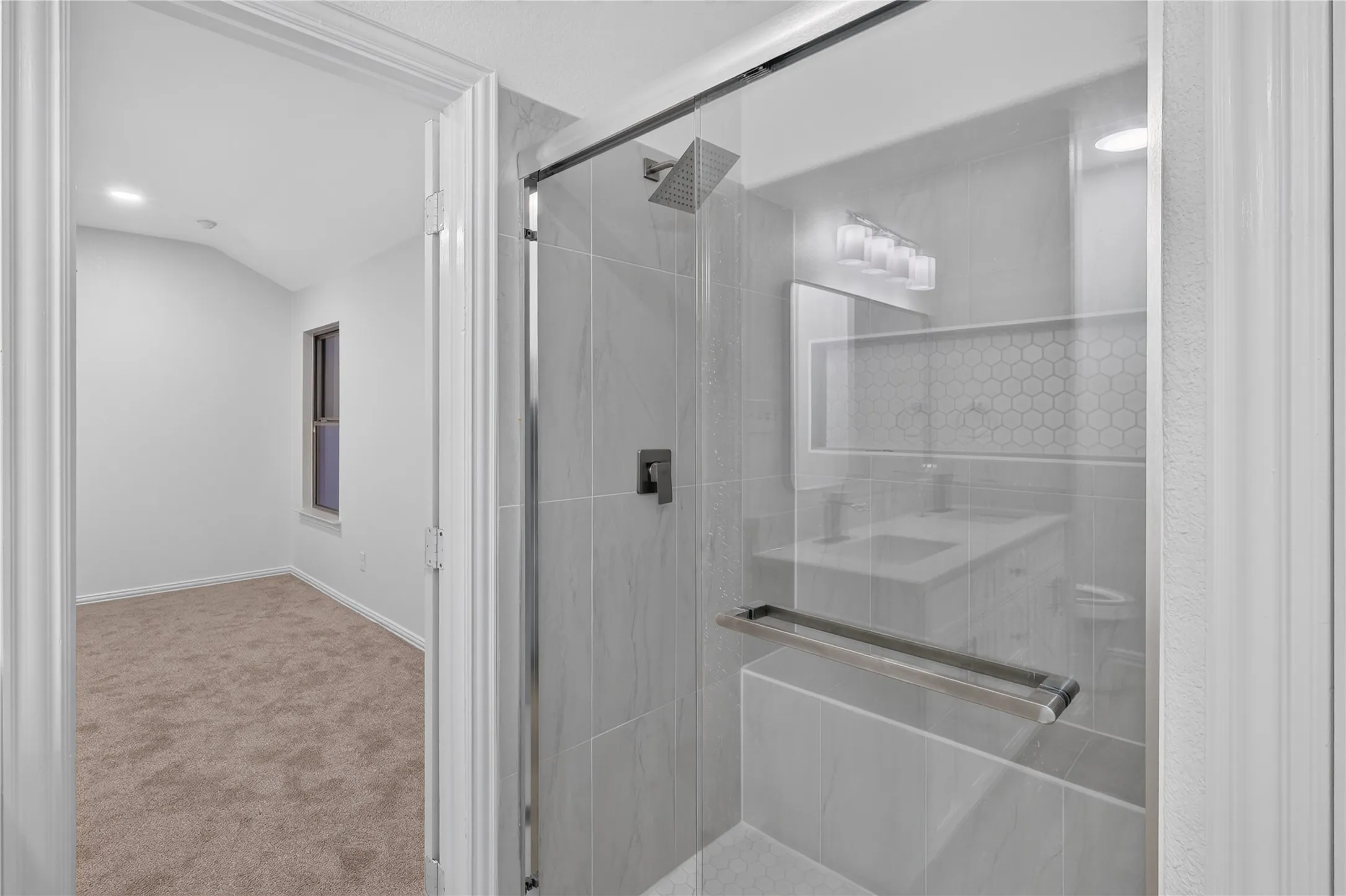 Glass-enclosed shower with a rainfall showerhead, large format tile surround, and a built-in shelf featuring honeycomb tile