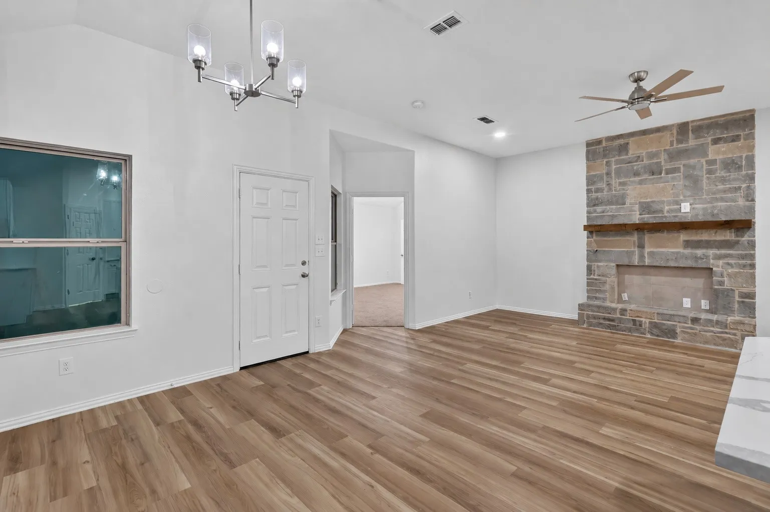 Vaulted ceiling with an attached chandelier, wood-finish flooring, stone fireplace with a wood mantel, and a ceiling fan