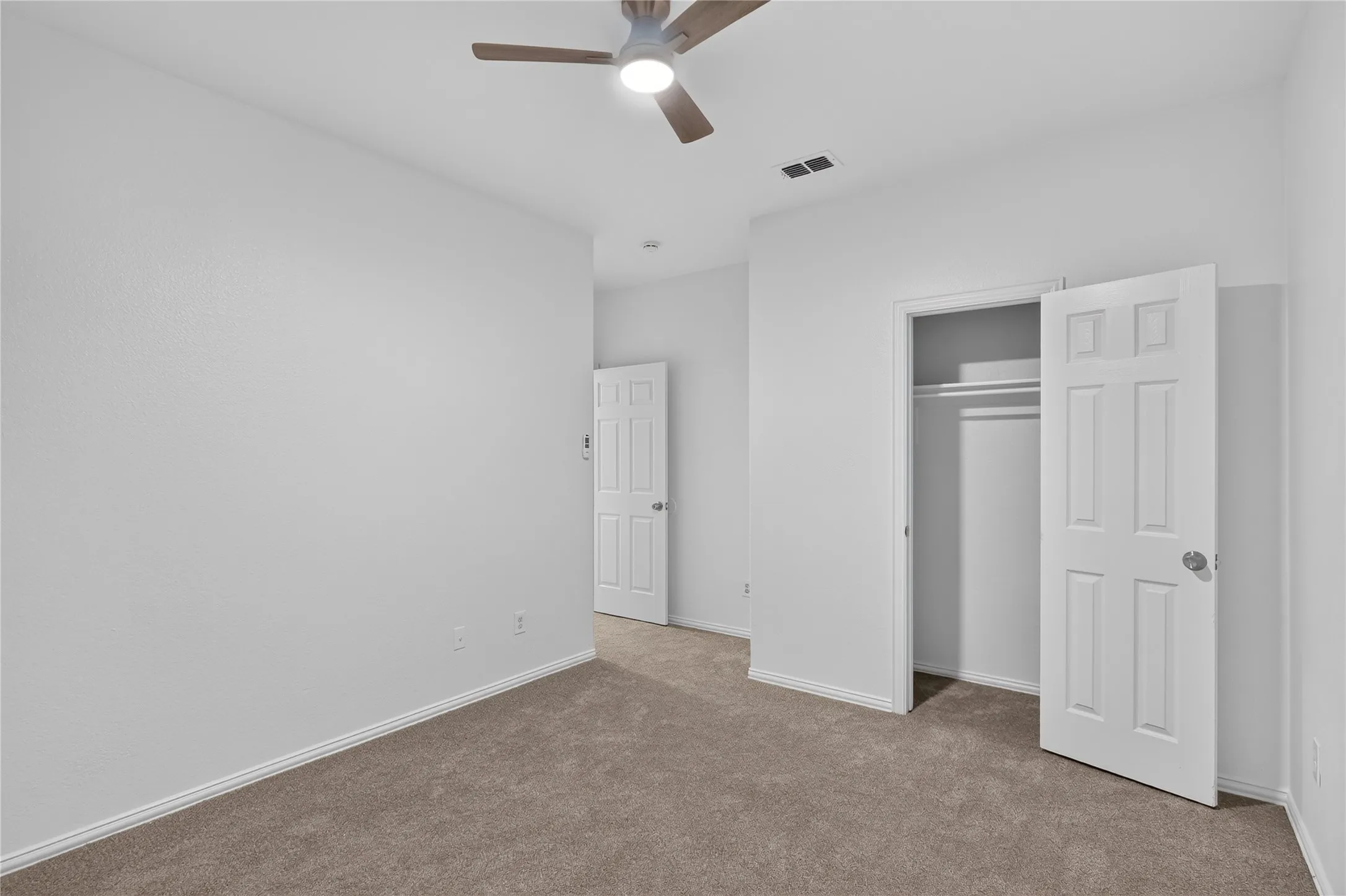 Spacious bedroom with neutral walls, wood-finish flooring, and ceiling fan