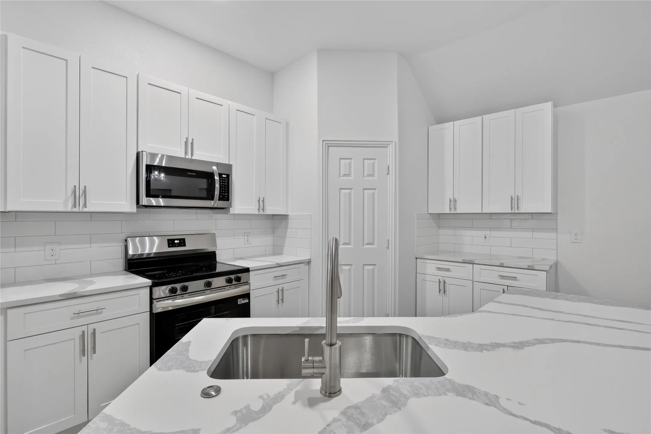 White cabinetry, subway tile backsplash, stainless steel appliances, stainless steel undermount sink, and light-toned countertops