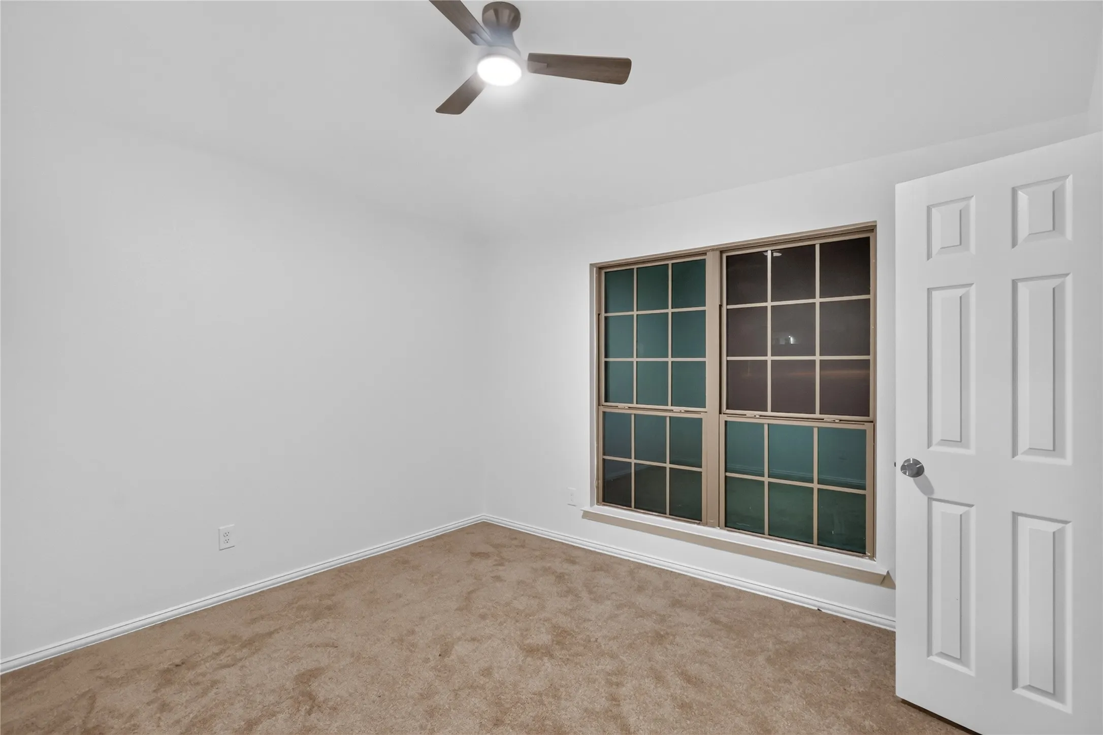 Neutral wall finishes, carpeted flooring, large grid windows, ceiling fan with integrated lighting, and a paneled door
