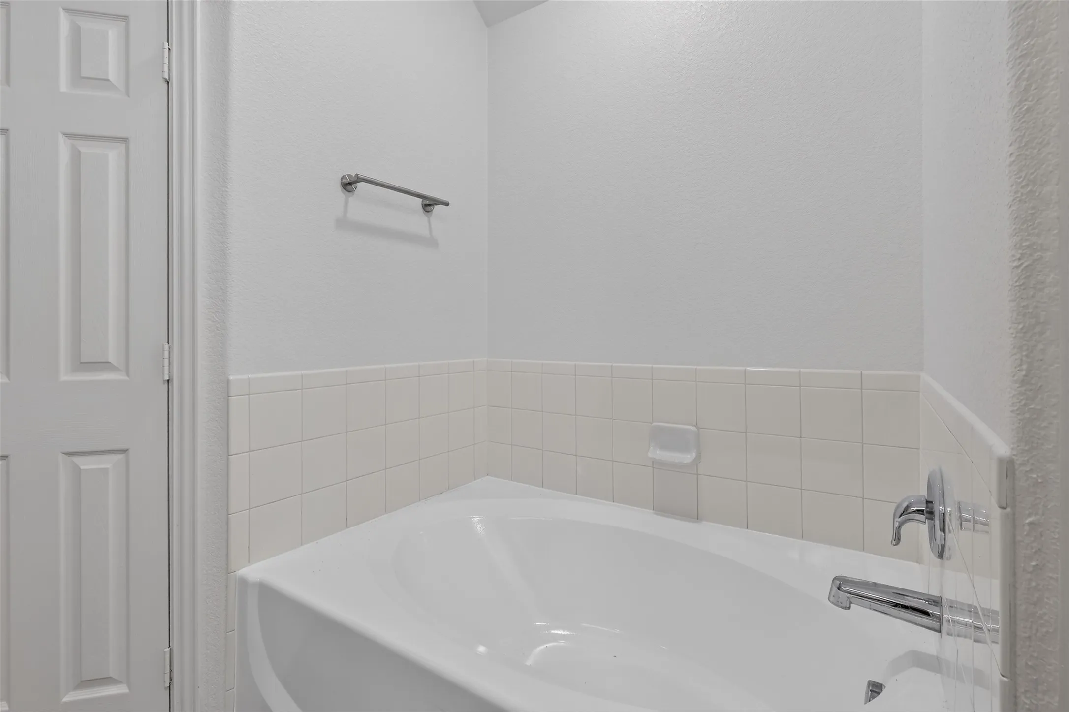 White soaking tub with chrome fixtures and white tiled surround