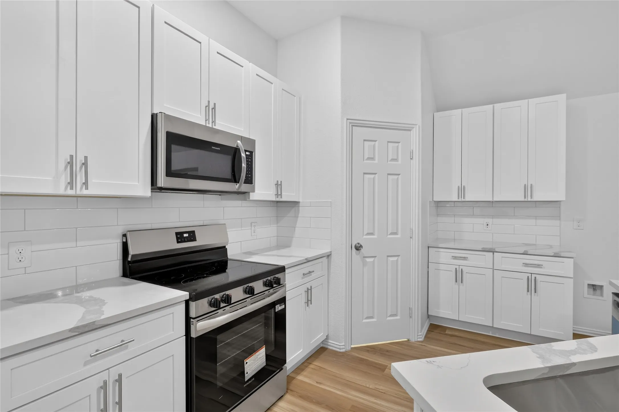 Kitchen featuring white shaker cabinetry, stainless steel appliances, white subway tile backsplash, light-toned wood-finish flooring, and light-toned countertops
