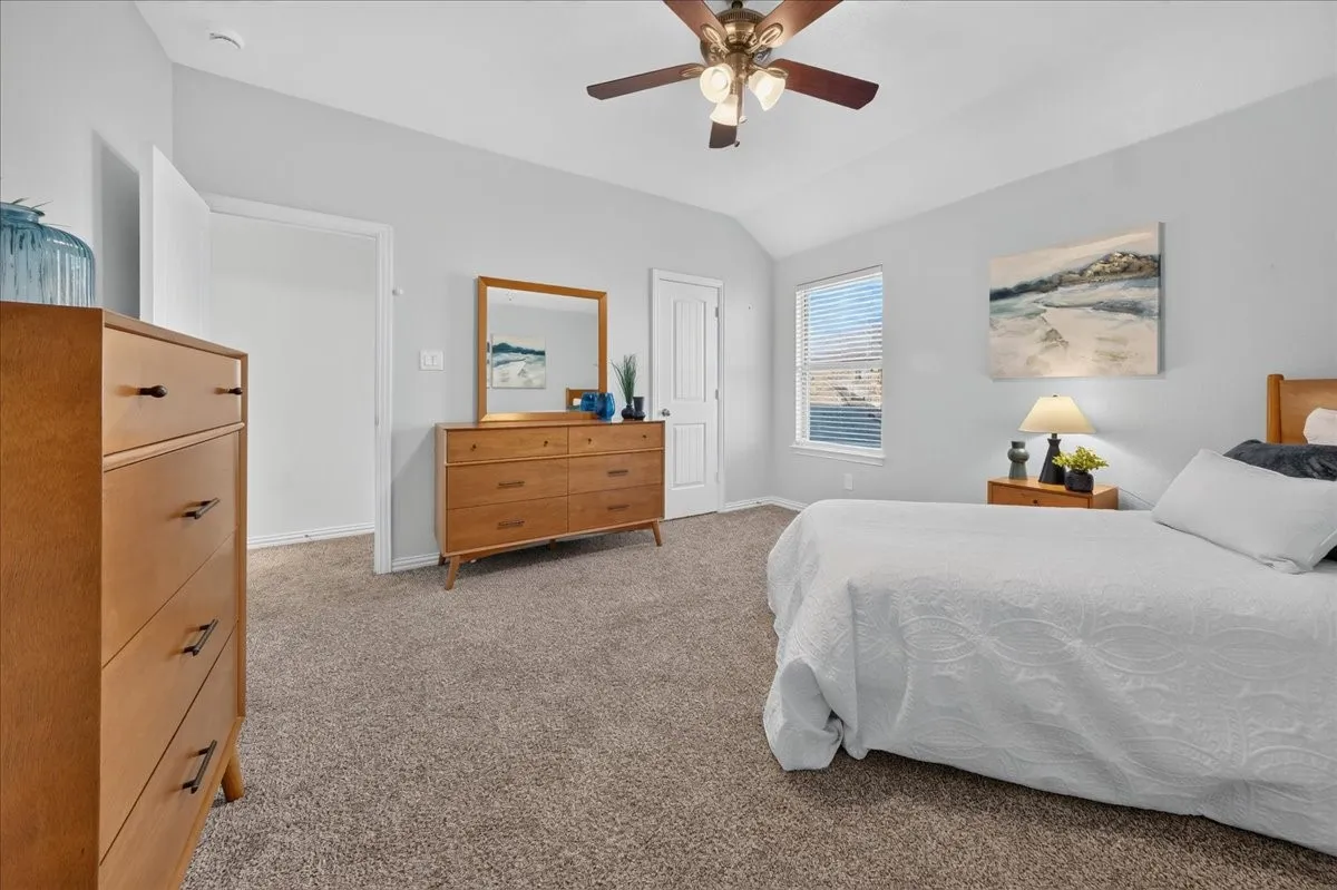 Vaulted ceiling with a ceiling fan, light-colored carpet, large window with blinds, and white interior doors