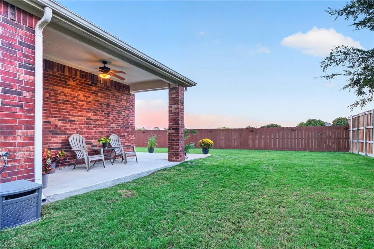 Expansive backyard featuring a covered patio, brick exterior, ceiling fan, and a wood privacy fence