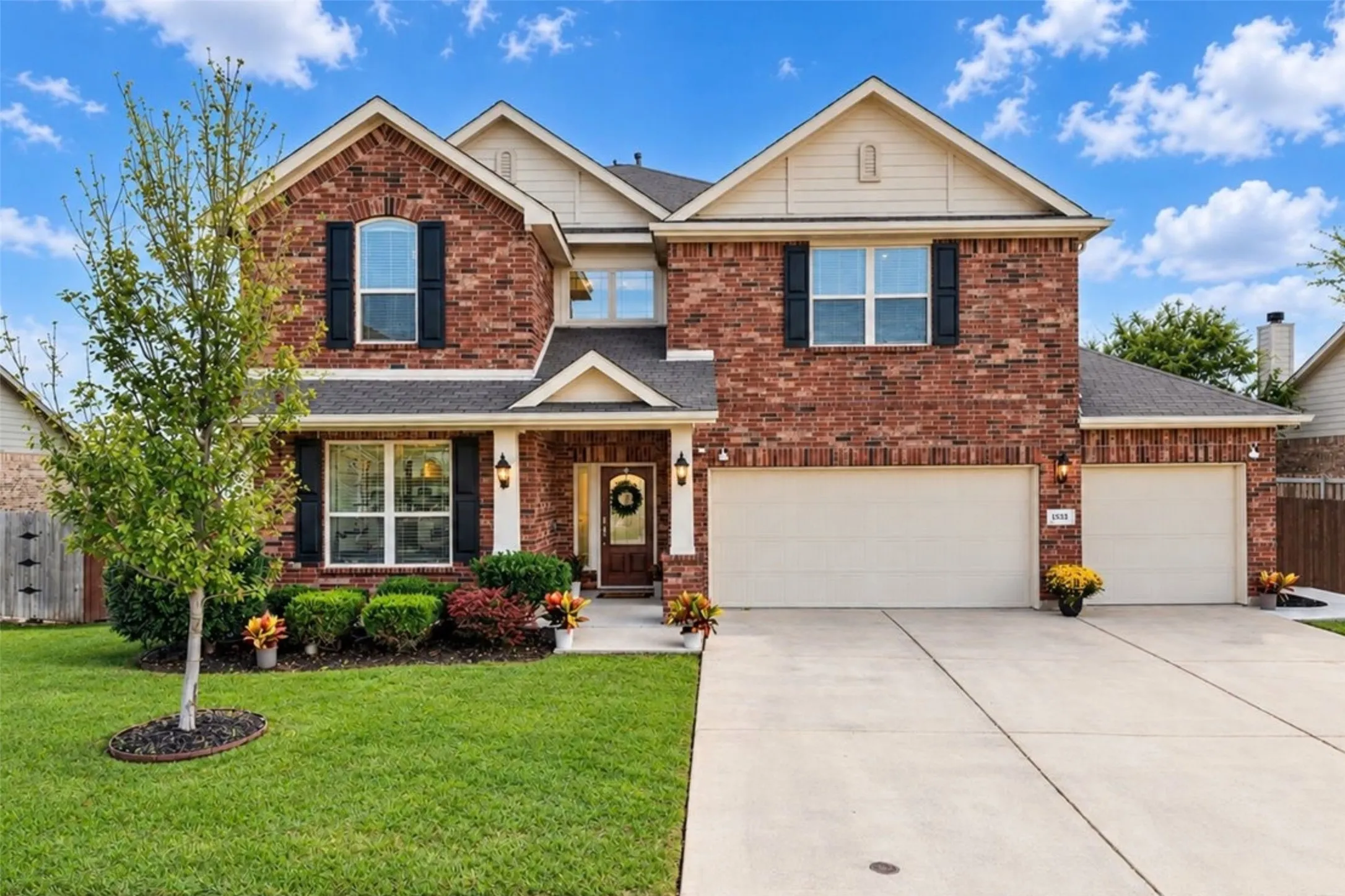 Brick facade, attached two-car garage, concrete driveway, front entry porch, and manicured landscaping