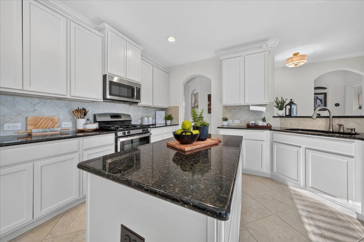 White shaker-style cabinetry, dark speckled countertops, stainless steel appliances, and a diagonal tile backsplash