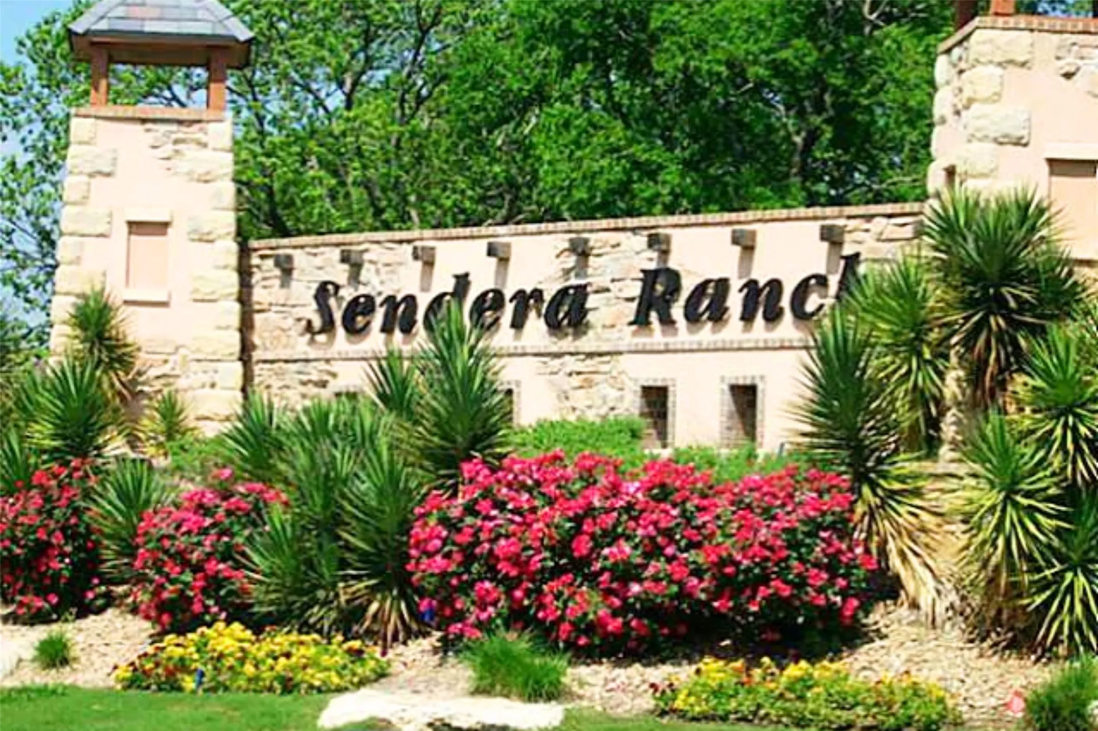 Stone-clad entry monument with a decorative turret and lush landscaping