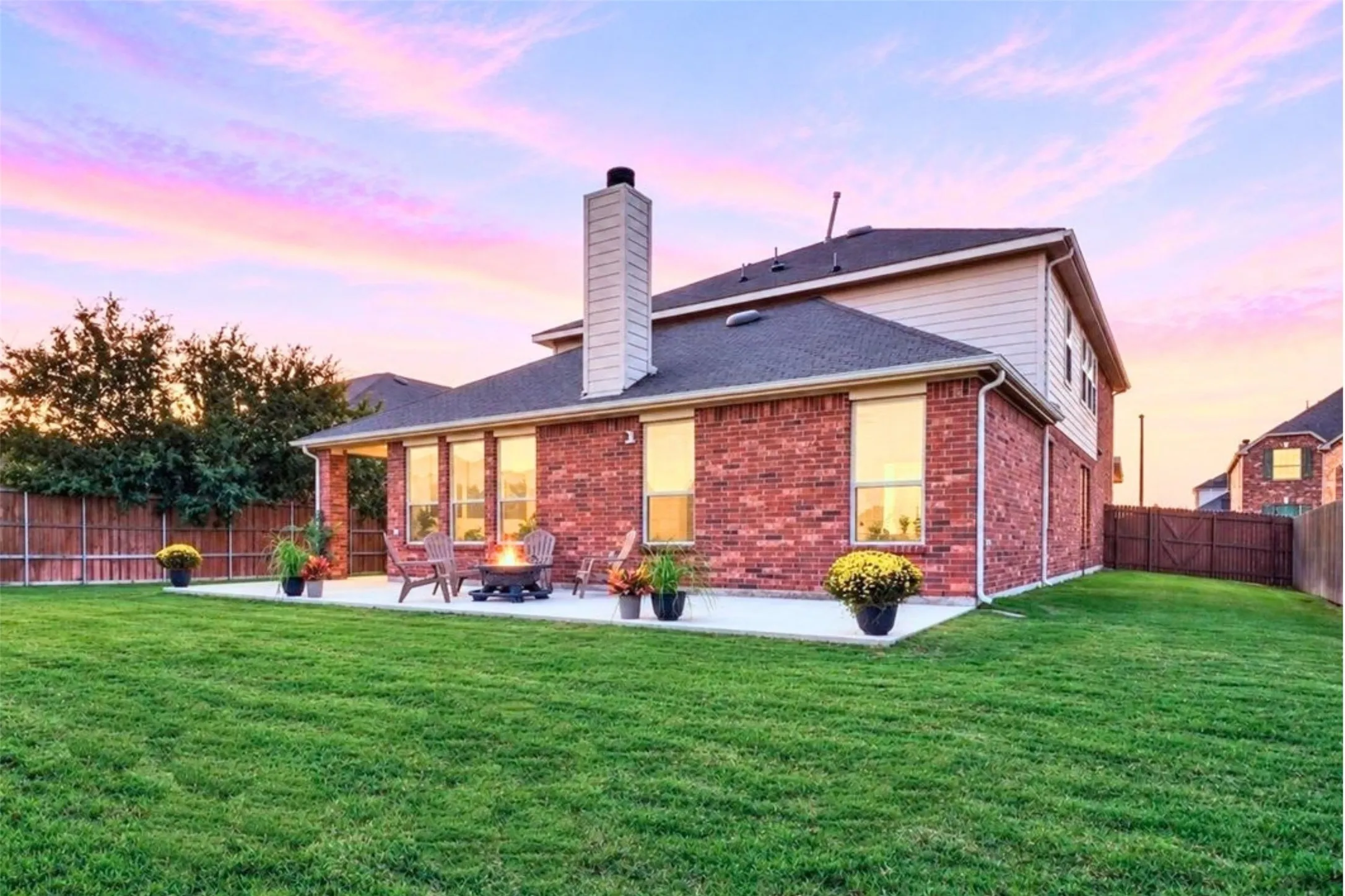 Expansive green lawn with a concrete patio, brick exterior, and a covered back porch