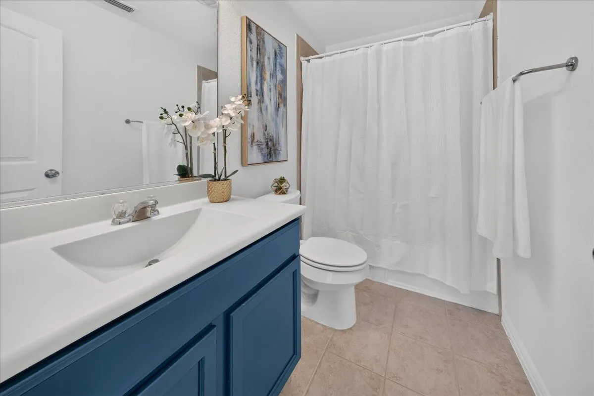 White vanity countertop with an integrated sink, blue-painted vanity cabinetry, and neutral-toned tile flooring