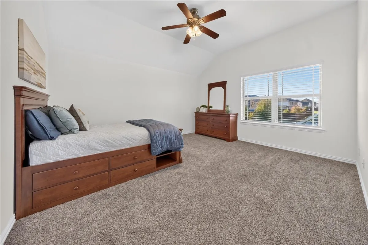 Vaulted ceiling with an attached ceiling fan, large window with blinds, and neutral carpeting