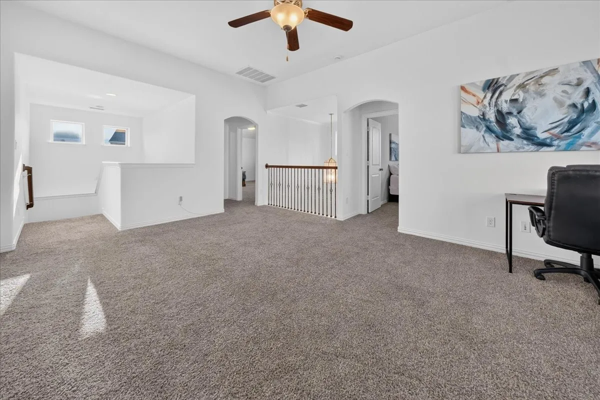 Carpeted floor, archways, white walls, ceiling fan, and staircase with wood handrail