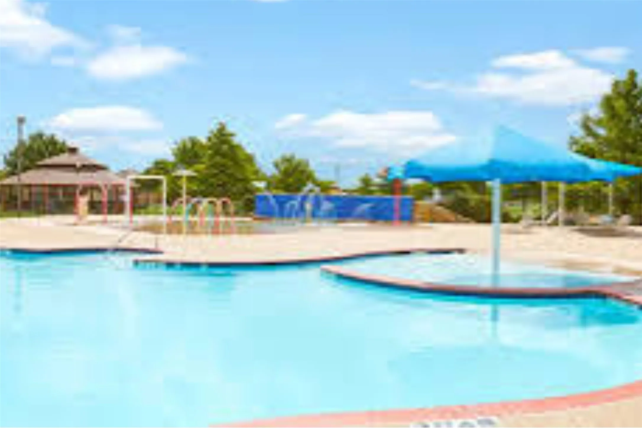 Resort-style community pool featuring crystal-clear water, multiple lap lanes with lane dividers, sun deck with ample lounging space, mature landscaping with shade trees, and adjoining recreational facilities including a covered pavilion and playground equipment