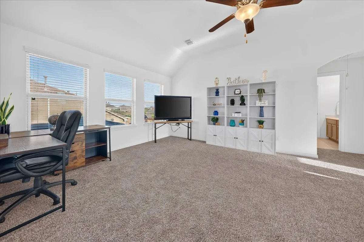 Vaulted ceiling with a ceiling fan, multiple windows with blinds, and carpet flooring