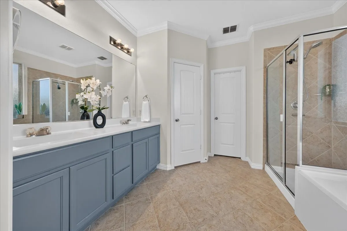 Dual vanity with white countertops, expansive wall mirror, and a glass-enclosed shower with tiled walls