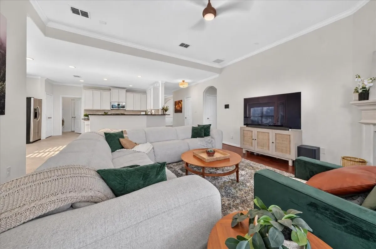 High vaulted ceiling, crown molding, wood-finish flooring, recessed lighting, and a kitchen with white cabinetry and dark countertops