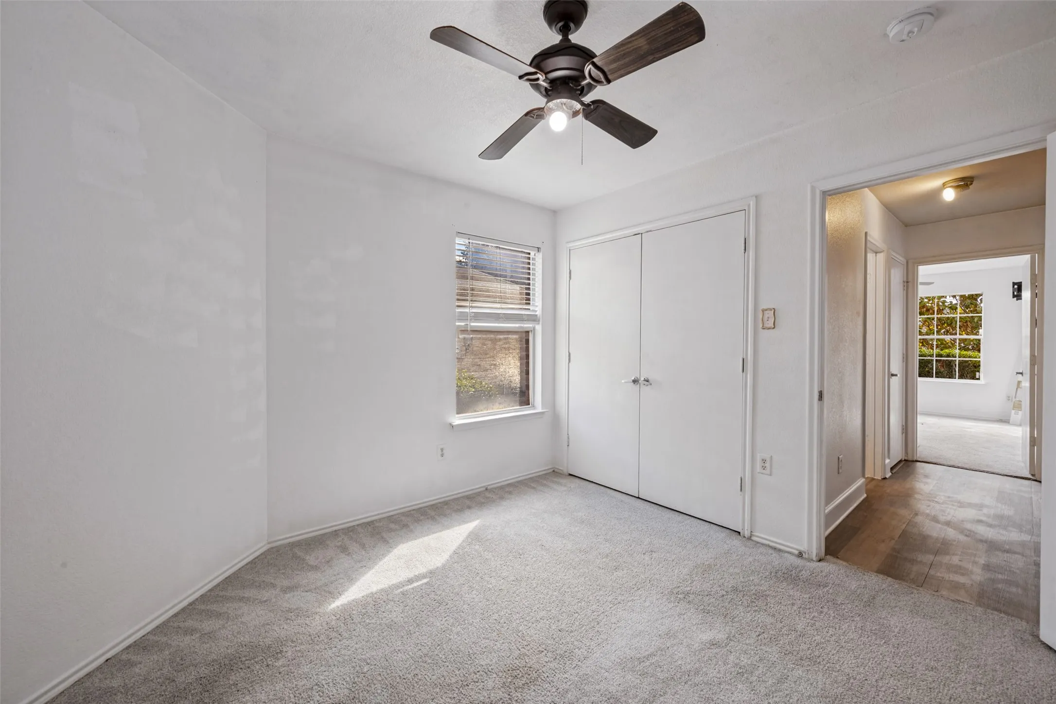 Recessed window with horizontal blinds, built-in double-door closet, ceiling fan with integrated lighting, and neutral carpet flooring