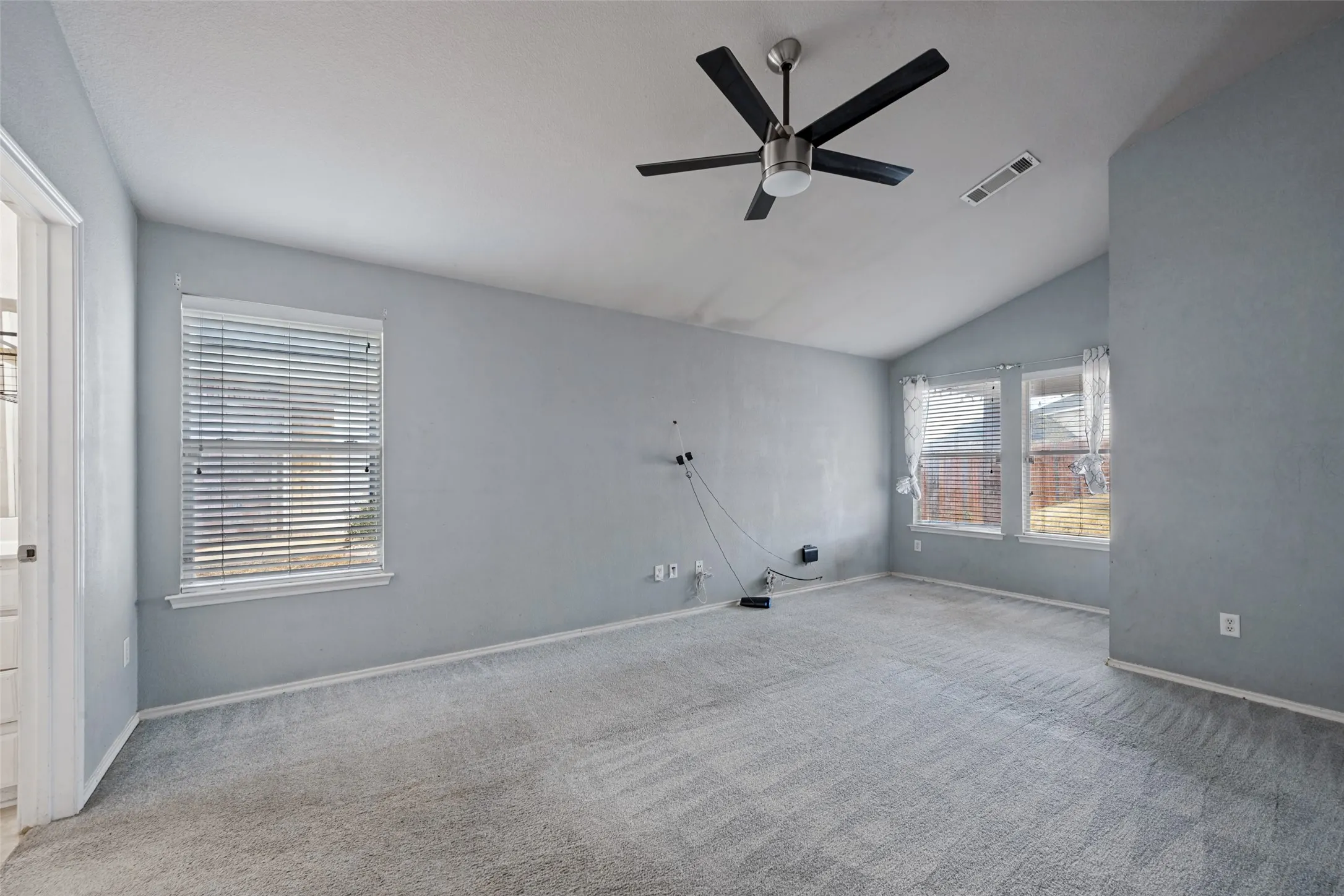 Vaulted ceiling with a ceiling fan, two windows, and neutral carpeting