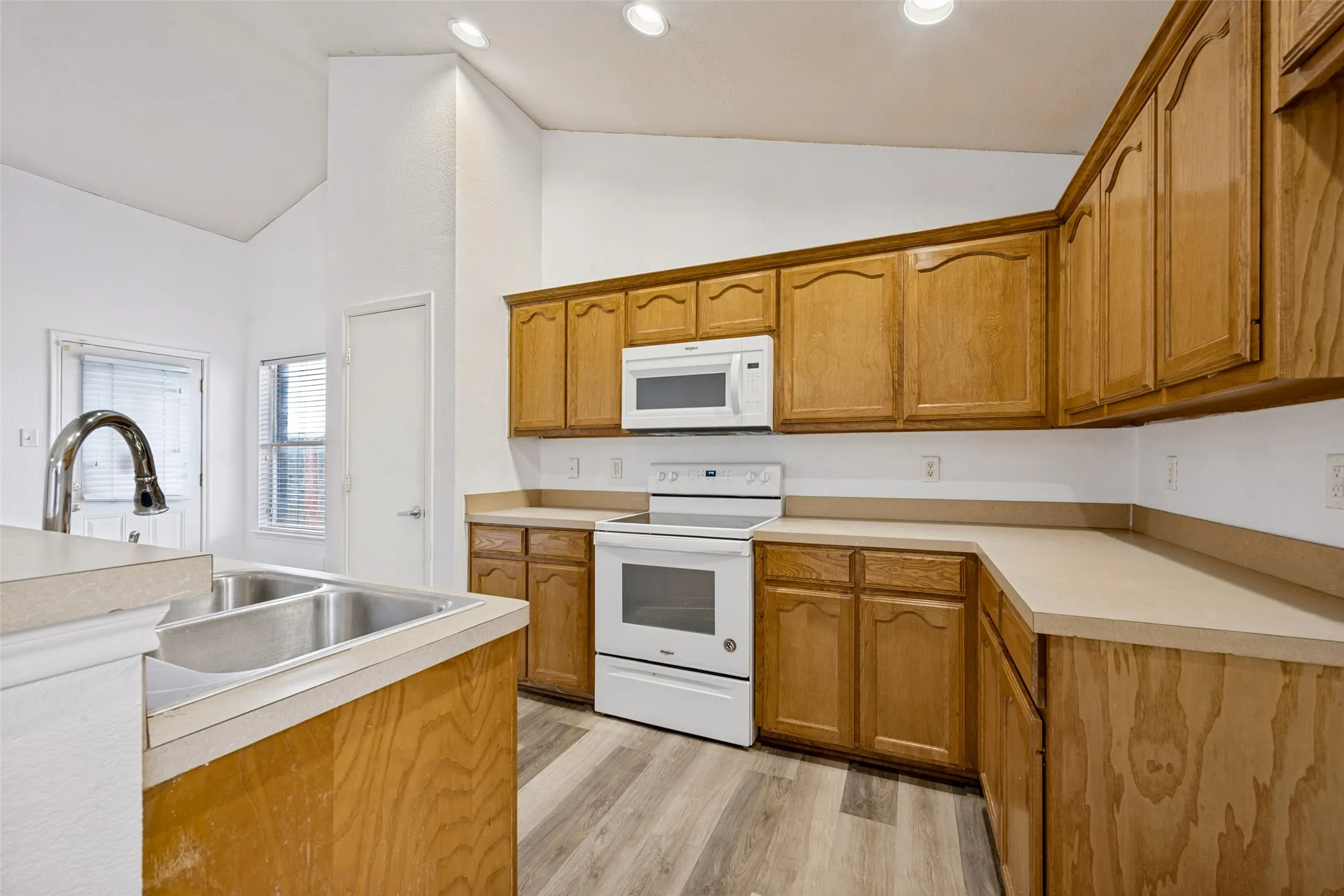 Kitchen featuring wood-finish cabinetry, light-toned countertops, a double basin stainless steel sink, and wood-finish flooring