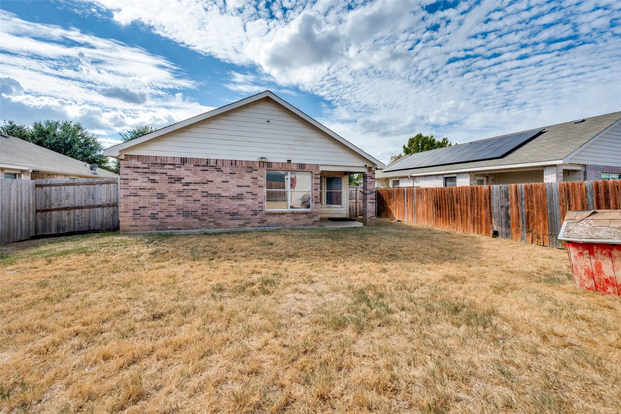 Brick exterior with siding gable, fenced perimeter, and rear patio access
