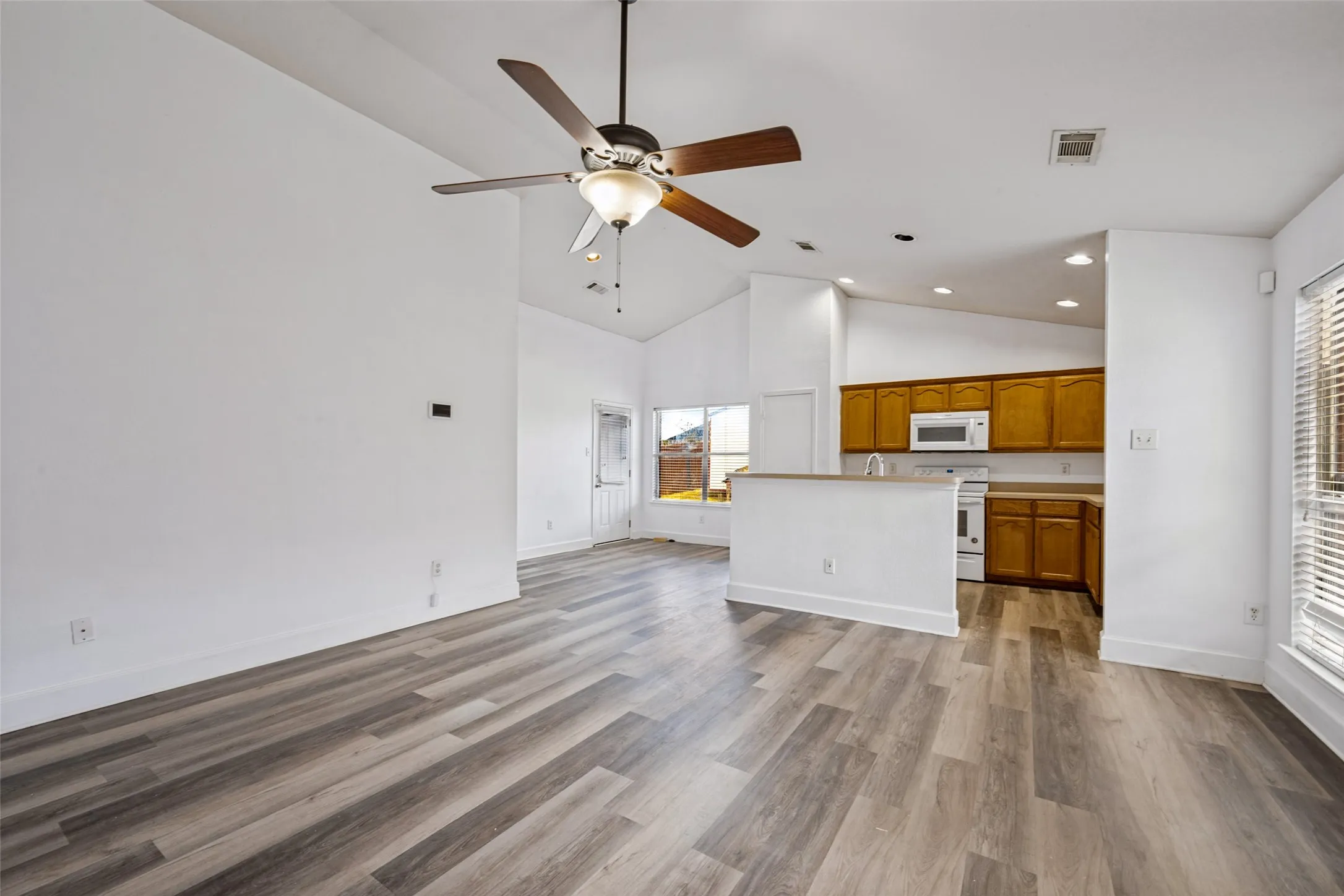 Vaulted ceilings, wood-finish flooring, ceiling fan, natural wood cabinetry, and white appliances