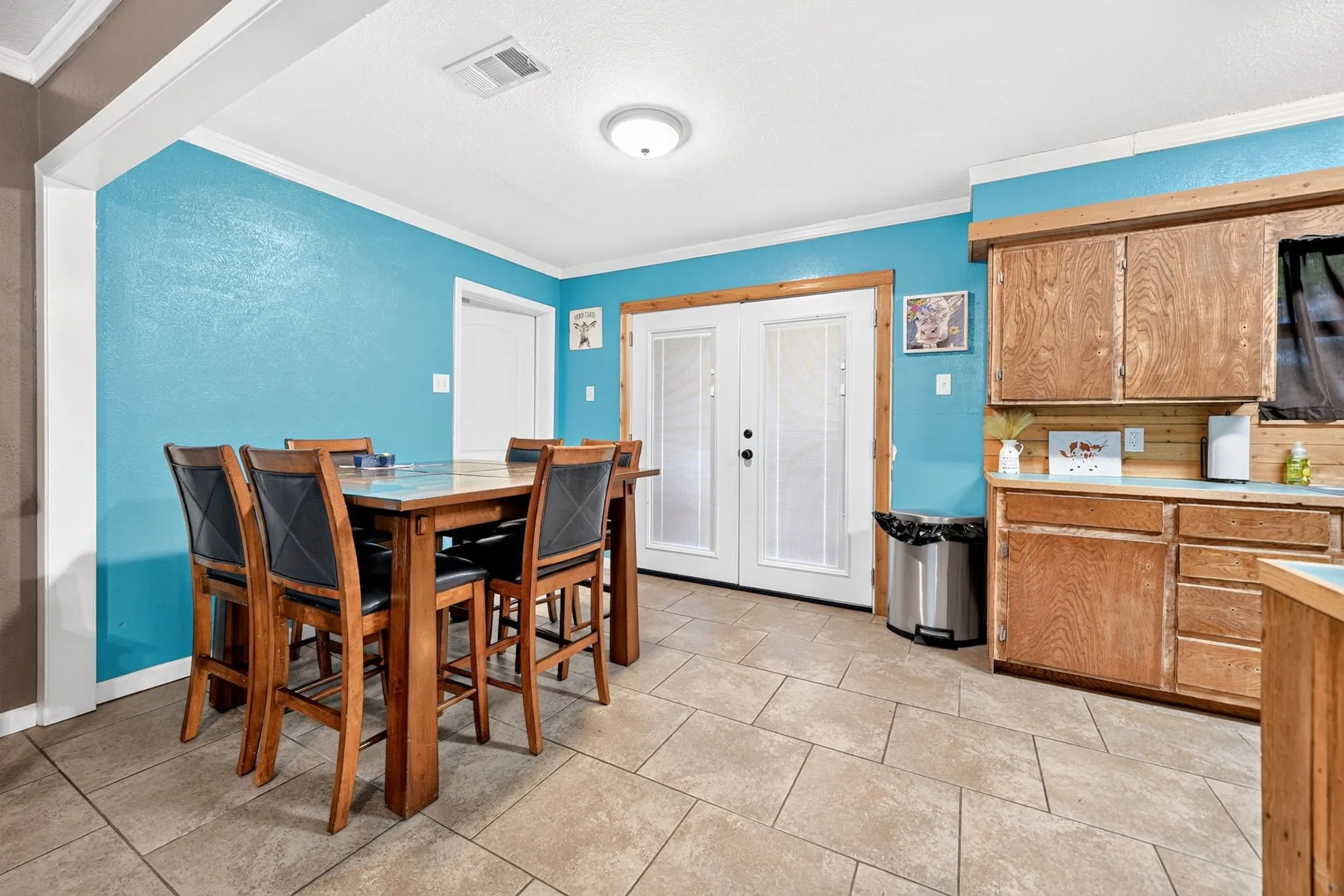 Tile flooring, wood-finish cabinetry, light blue walls, white trim, and white French doors