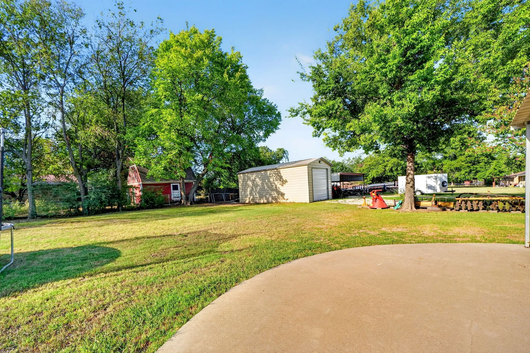 Expansive lawn with mature trees, a detached storage shed, and a concrete patio