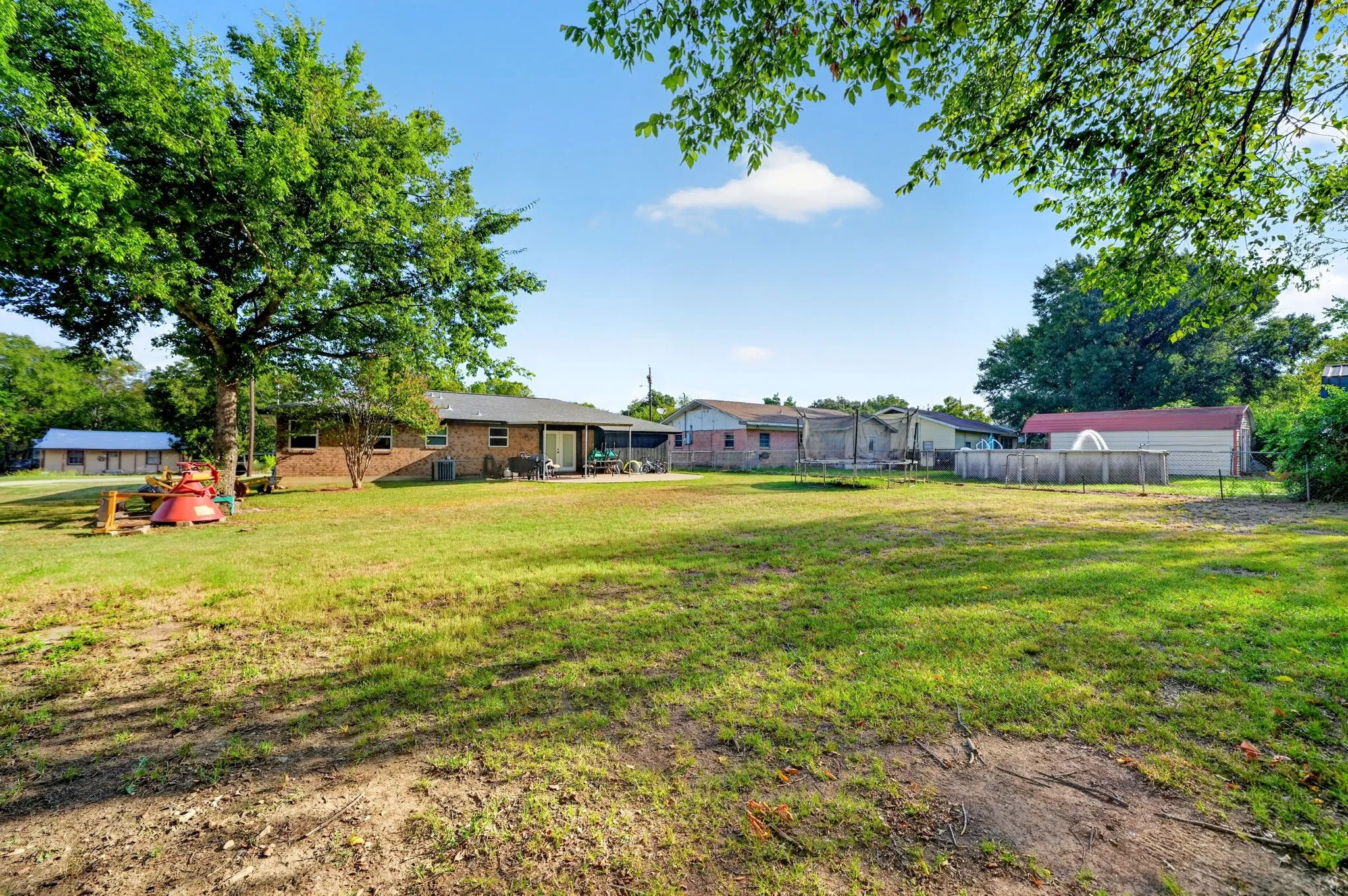 Expansive grassy yard area with mature trees, a brick-clad residence, and a fenced above-ground pool