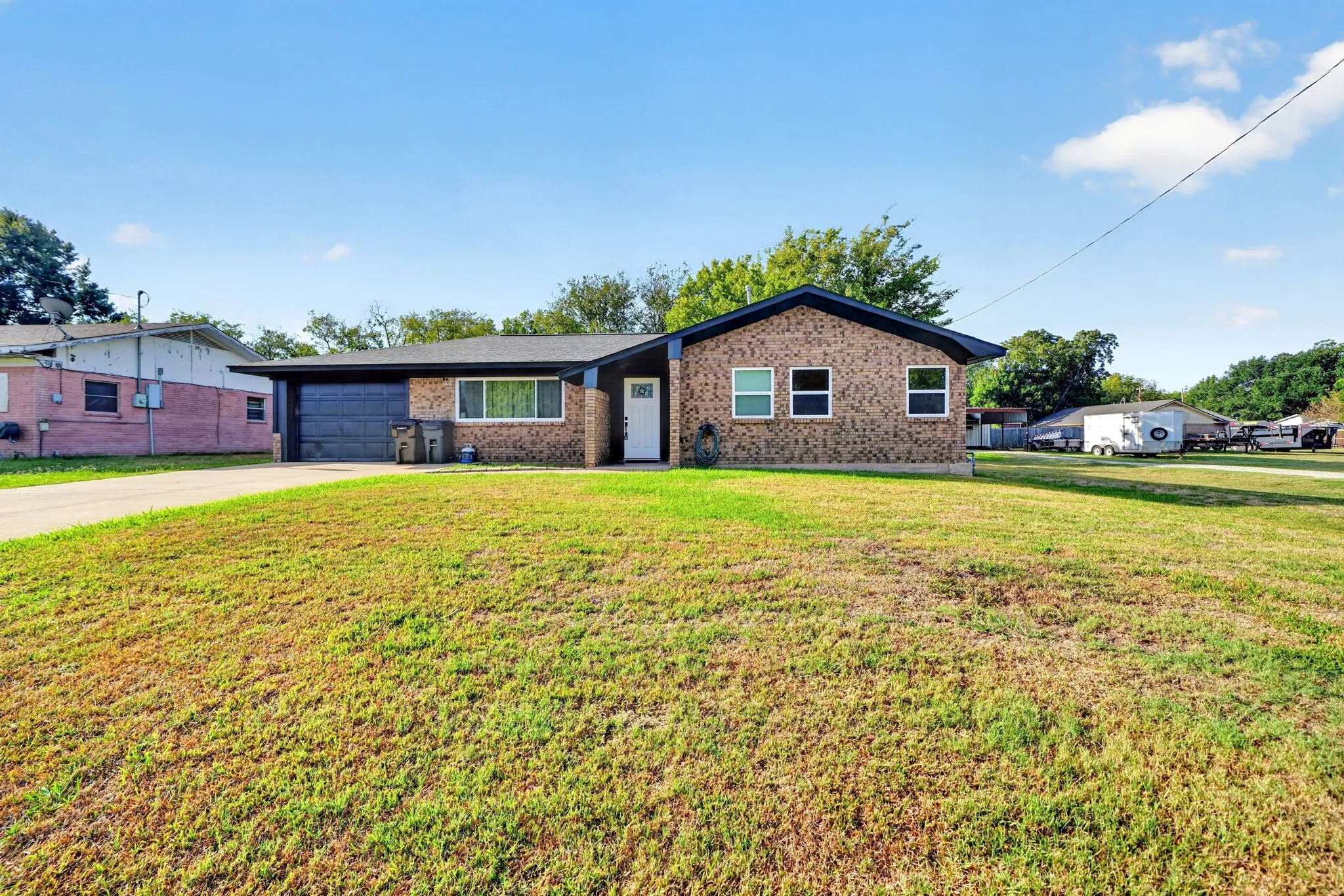 Brick facade home featuring a prominent front lawn, a single-car garage, and a concrete driveway
