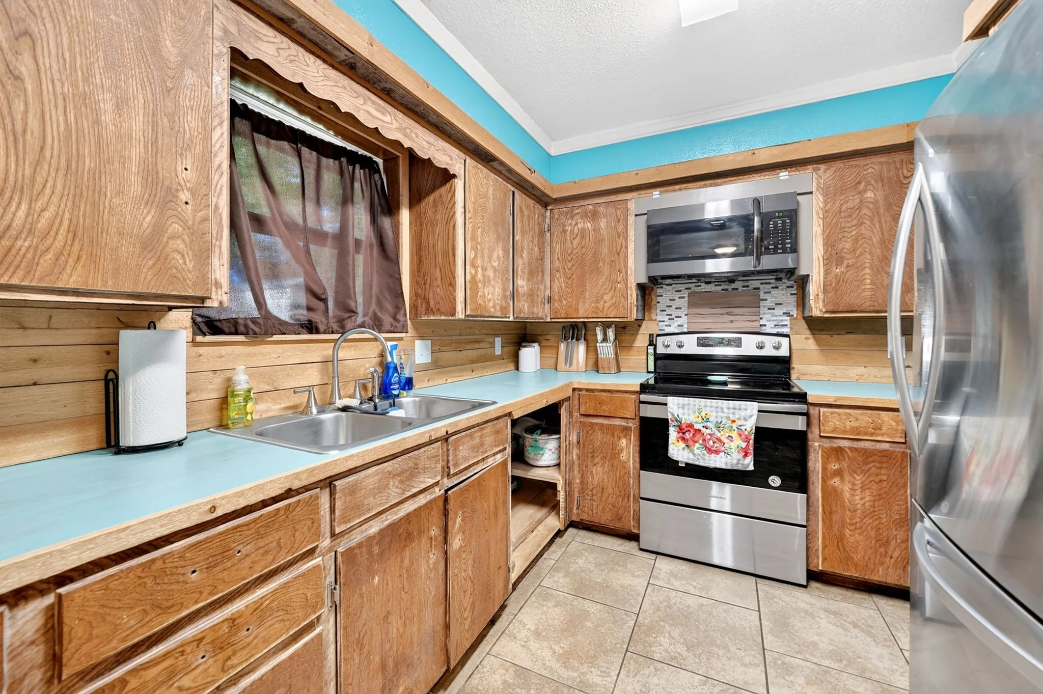 Wood-finish cabinetry, stainless steel microwave, stainless steel range, and tile flooring